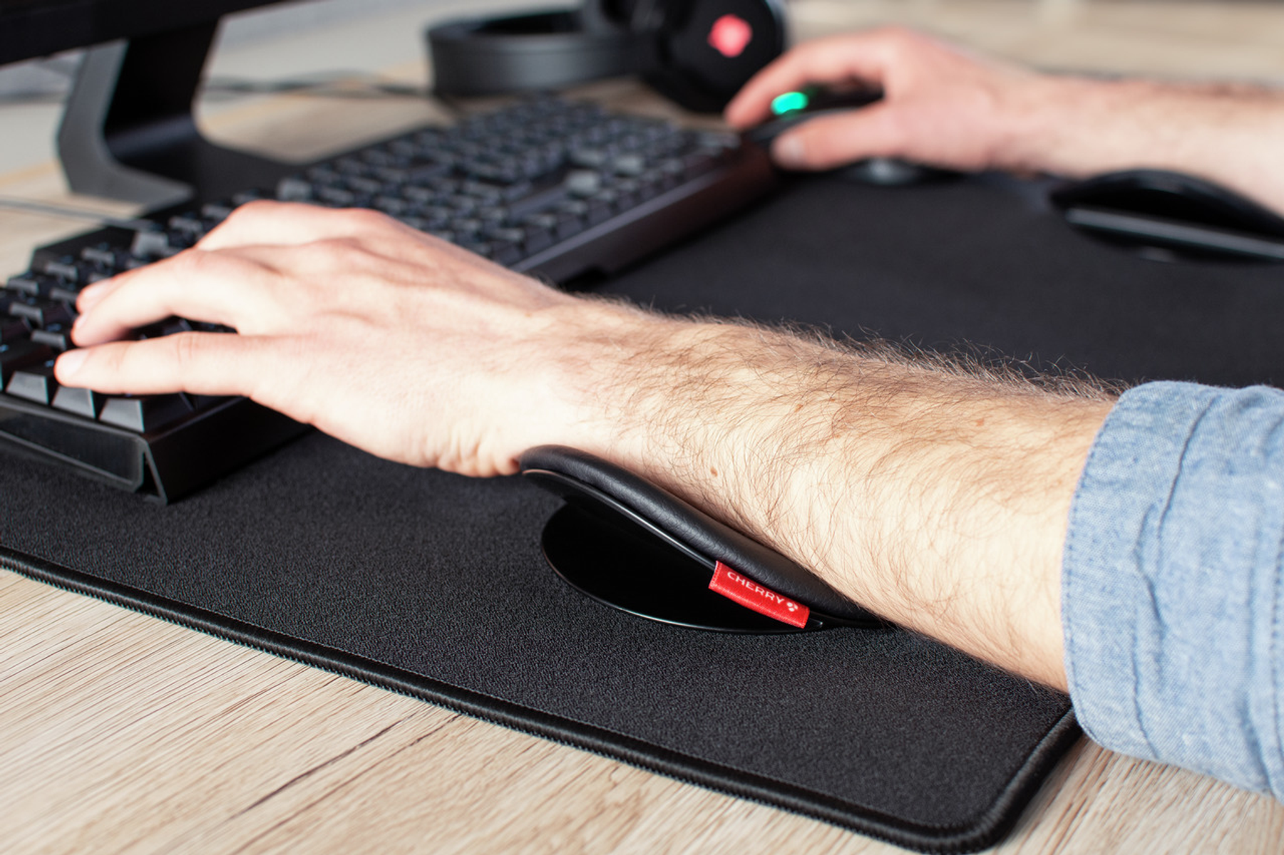 Eine Person, die einen Computer mit einer schwarzen Handgelenkstütze mit einem roten Cherry-Logo-Etikett auf einem schwarzen Mauspad benutzt.