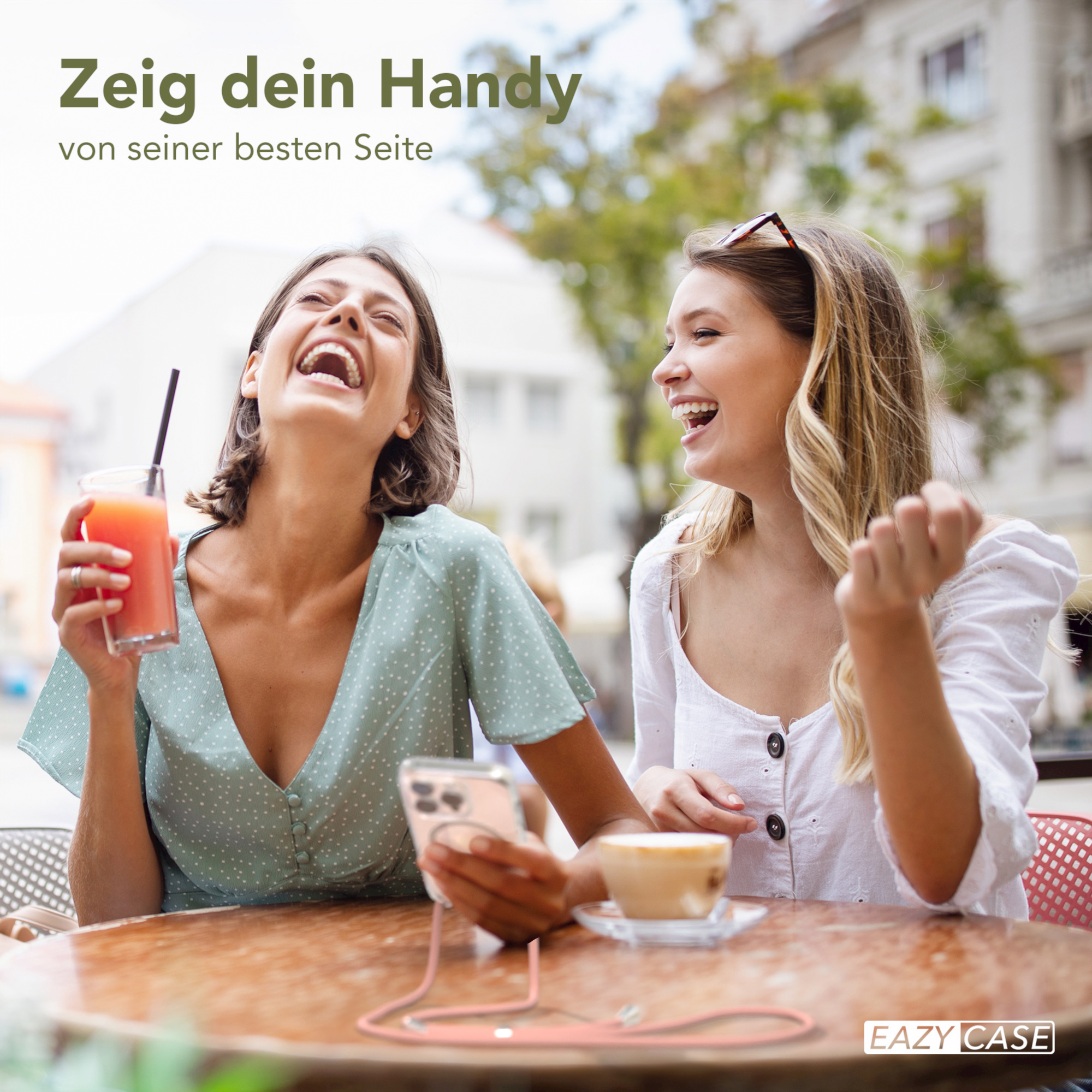 Zwei lachende Frauen, eine hält ein Telefon mit pinker Hülle und Gurt, draußen.