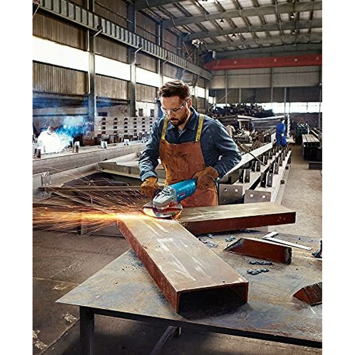 Ein Mann in einer Werkstatt benutzt einen Schleifer, Funken fliegen. Metall und Werkzeuge sind sichtbar.