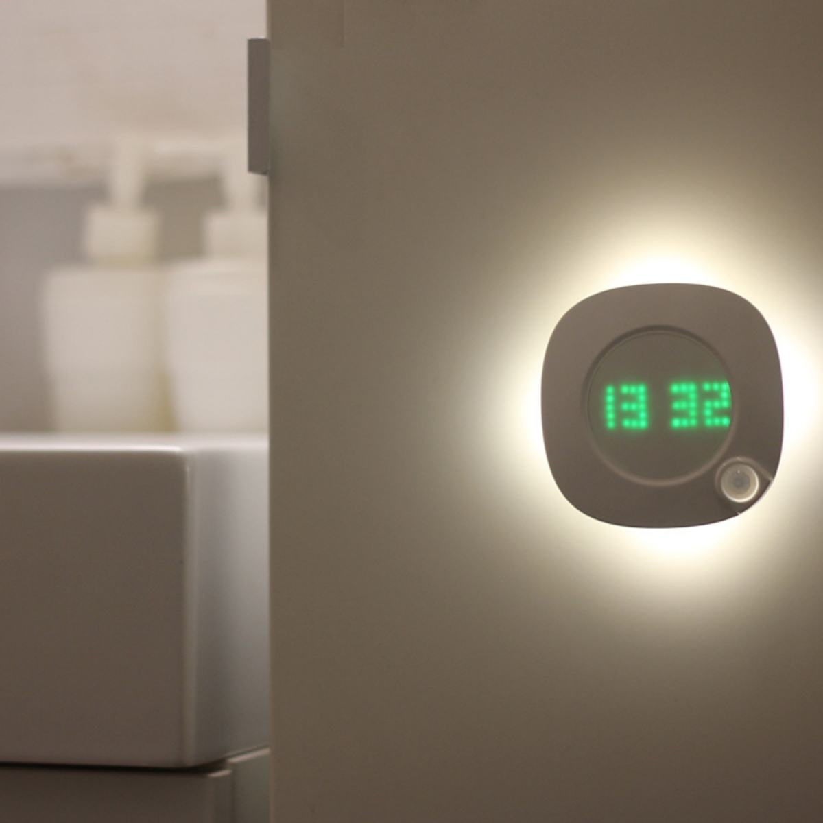 Rundes, weißes Nachtlicht mit grüner Digitaluhr an hellgrauer Wand.