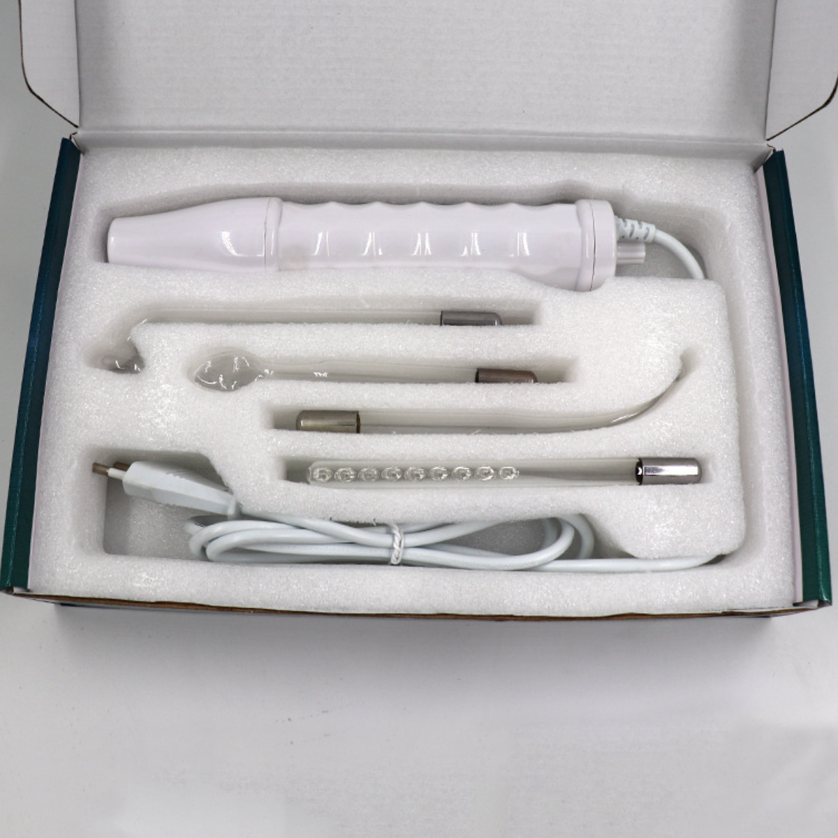 Ein Hochfrequenz-Hautpflegegerät in einer weißen Box. Enthält Glaselektroden und einen weißen Griff.