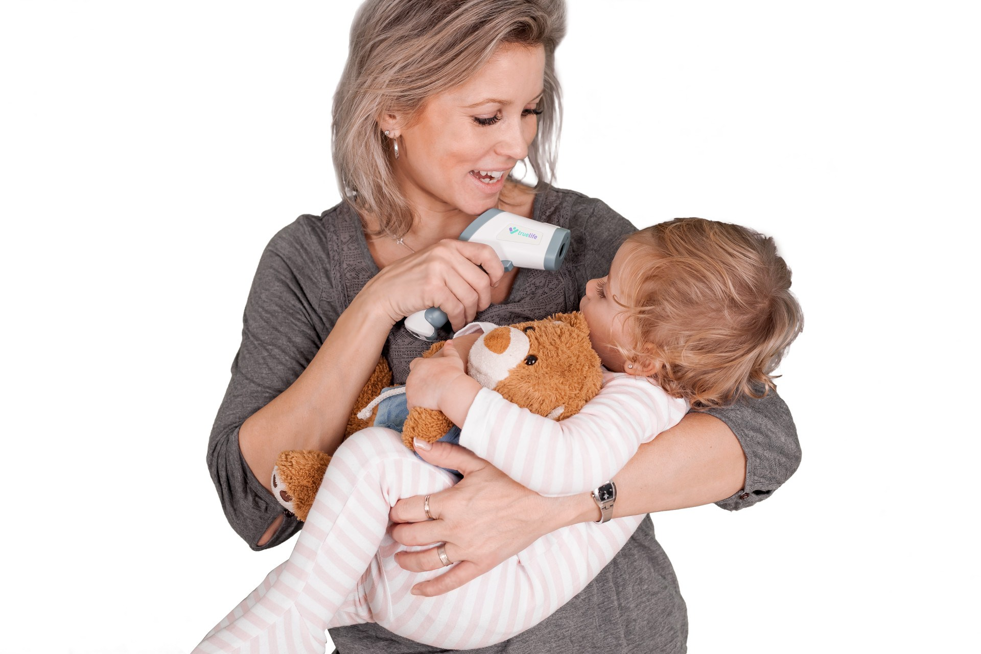 Eine Frau misst die Temperatur eines Kindes mit einem Thermometer. Teddybär im Arm.
