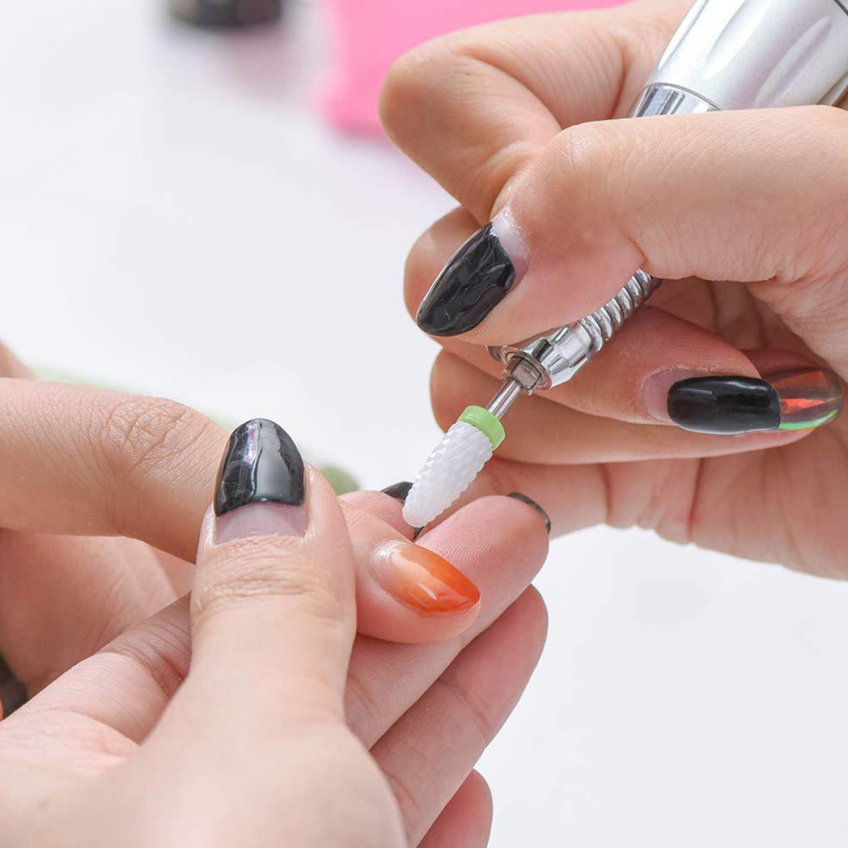 Eine Person, die einen Nagelbohrer an einem Nagel verwendet. Andere Nägel und Werkzeuge sind ebenfalls sichtbar.