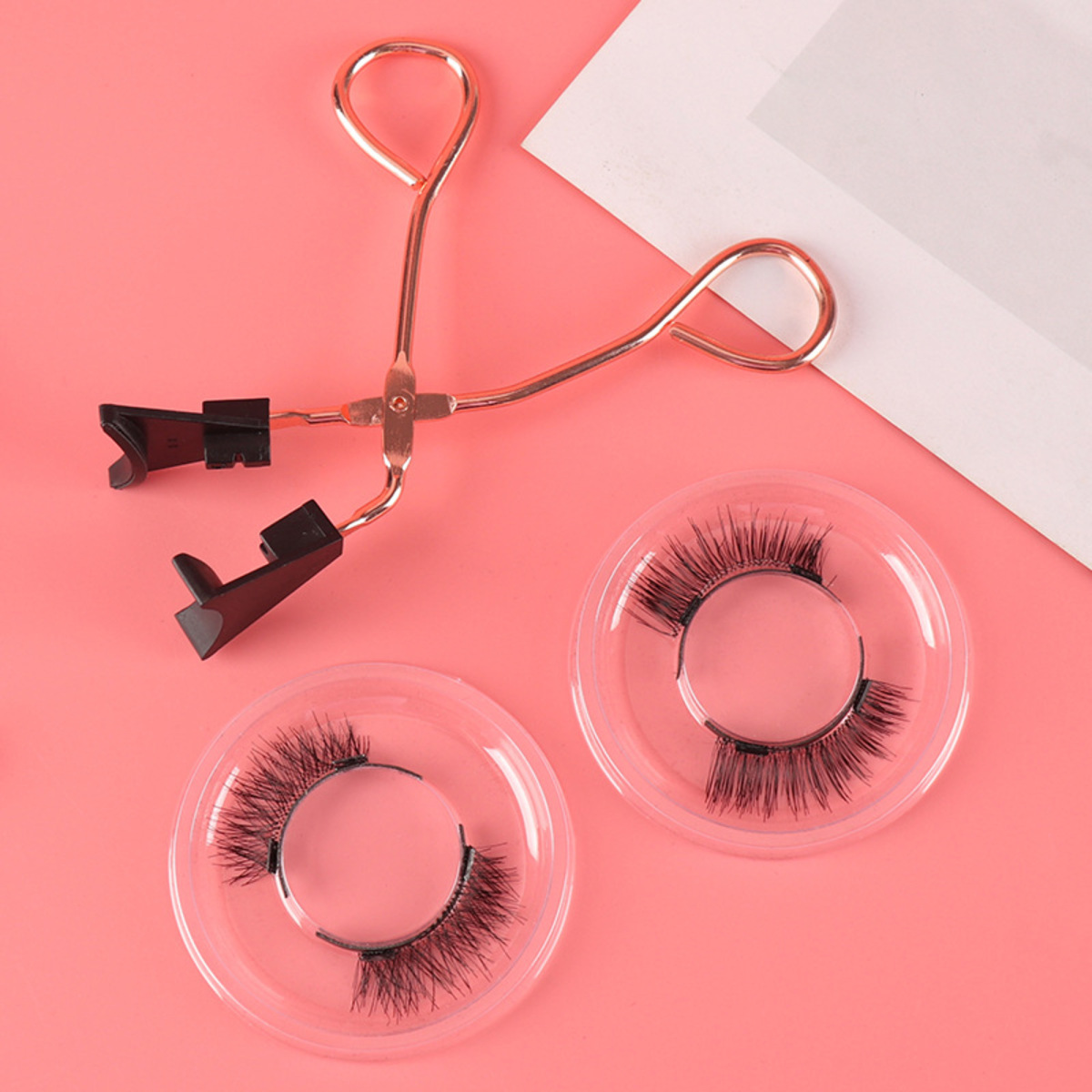 Wimpernzange mit zwei Sätzen falscher Wimpern auf pinkem Hintergrund.