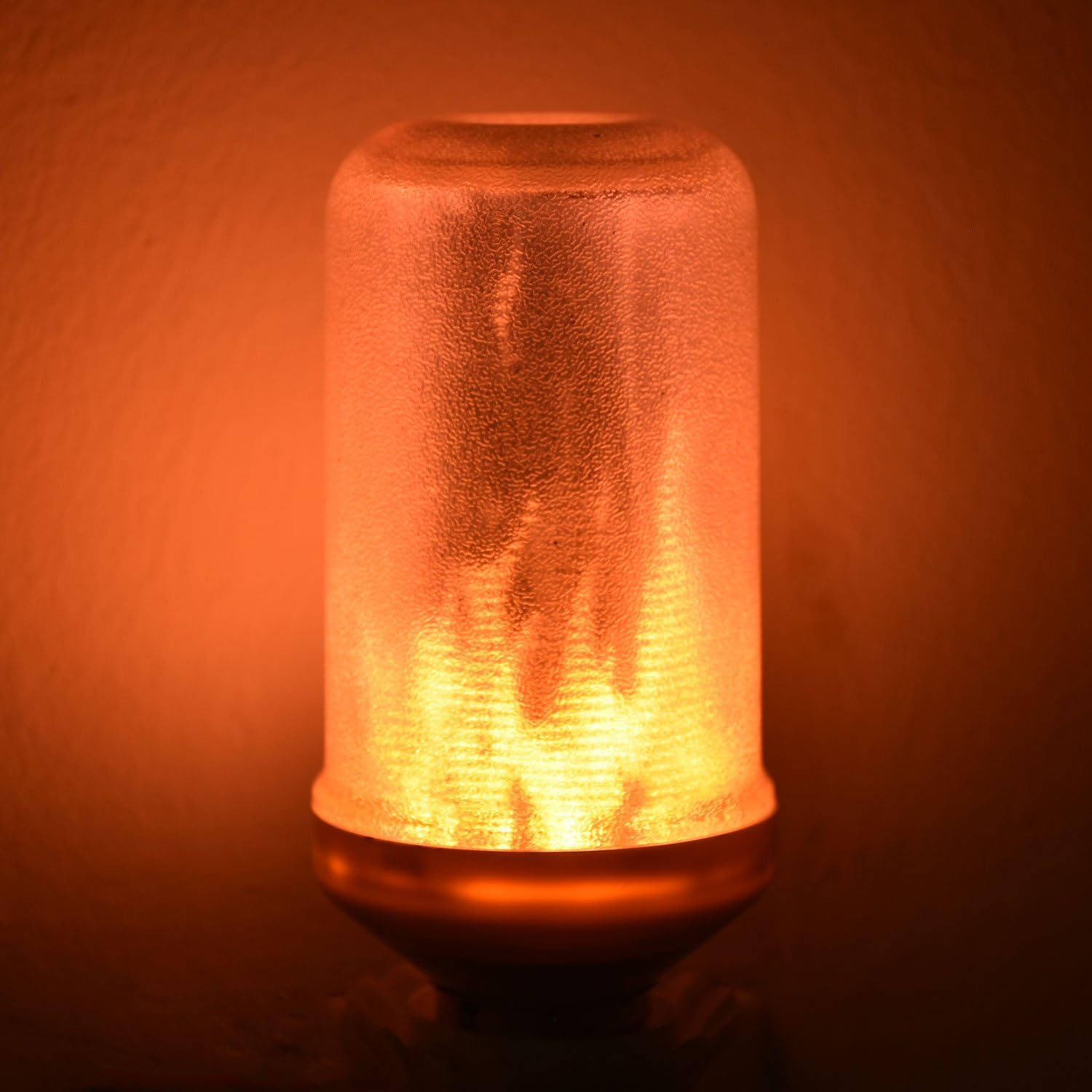 Eine flammenförmige Leuchte leuchtet orange und gelb. Die Leuchte hat eine strukturierte Glasabdeckung und einen Metallsockel.