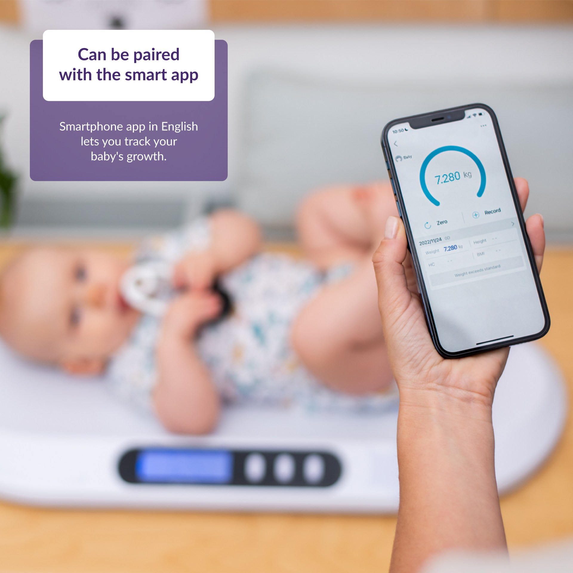 Ein Baby liegt auf einer Waage mit einem Telefon, das das Gewicht anzeigt. Der Hintergrund ist ein verschwommener Raum.