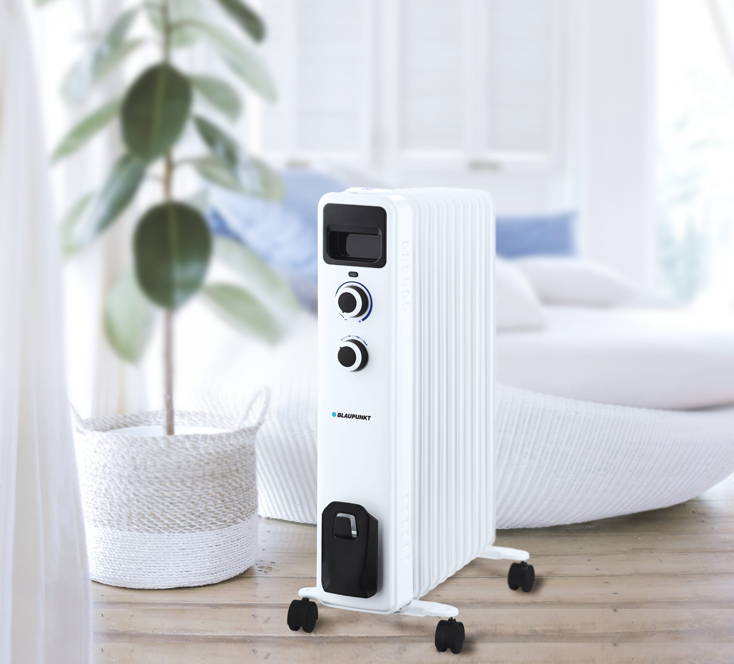 Un termoventilatore elettrico bianco su un pavimento in legno con una pianta e una finestra sullo sfondo.
