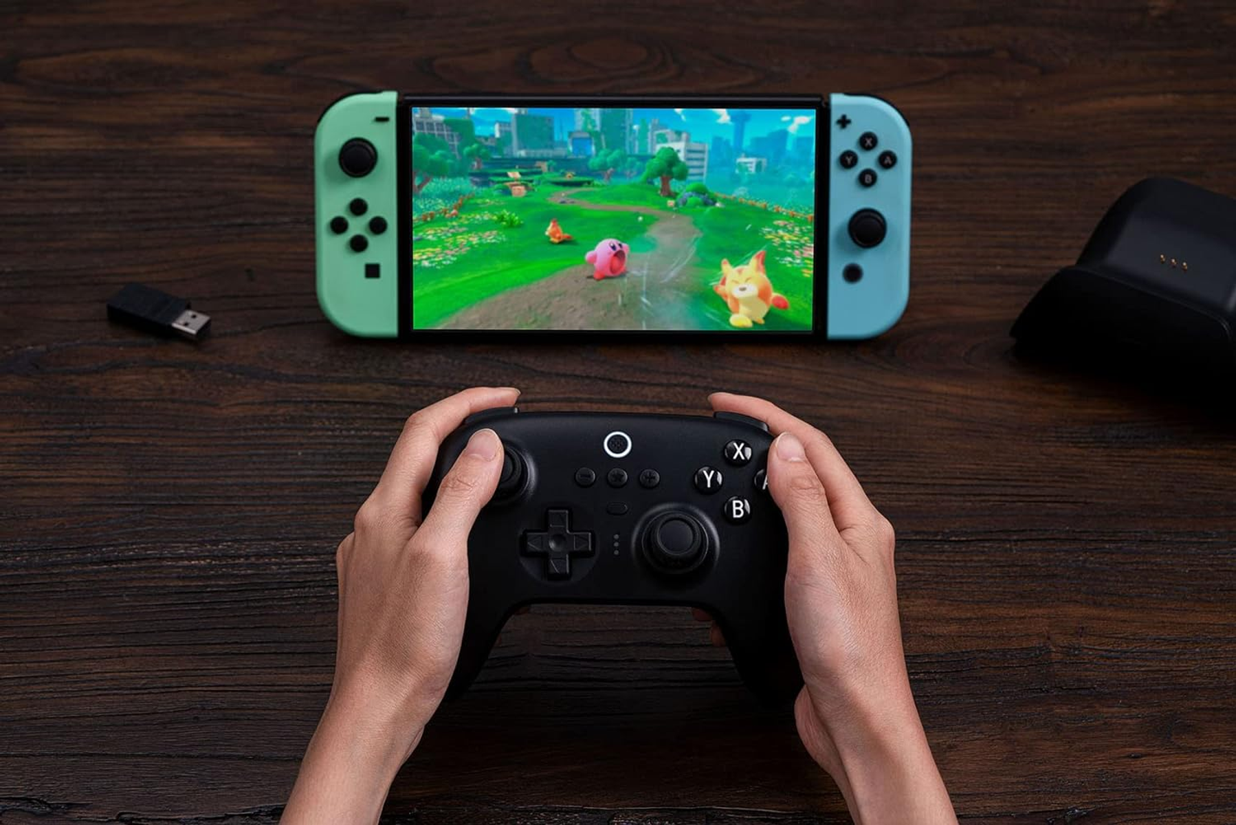 Dłonie trzymające czarny kontroler do gier. W tle Nintendo Switch, pokazujący ekran gry.