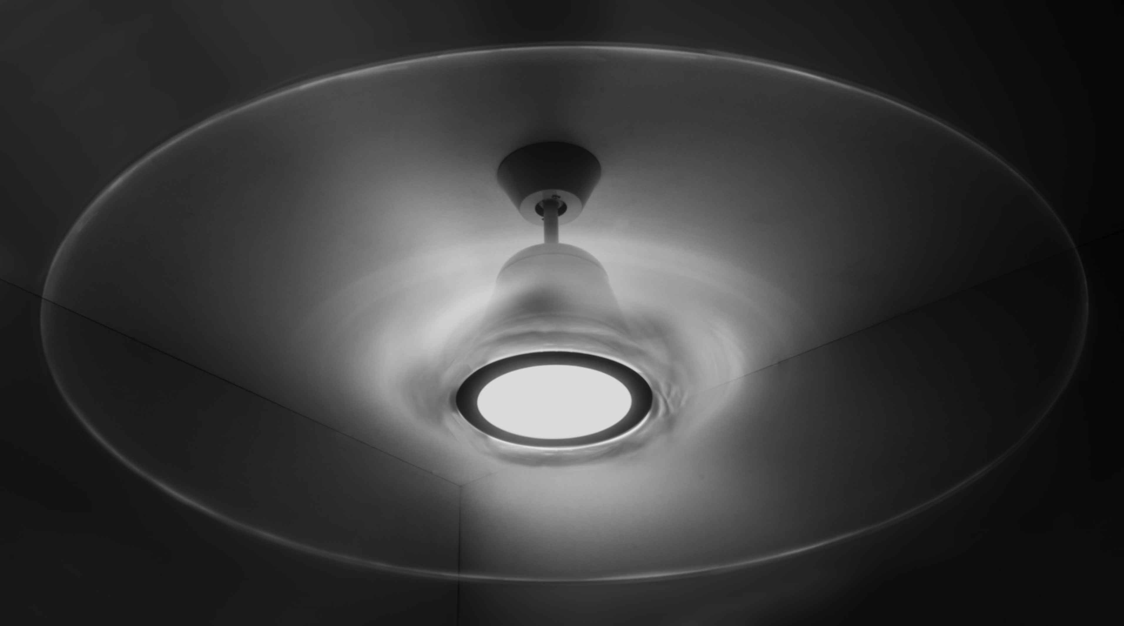 Deckenventilator in Bewegung. Rotorblätter sind durch Bewegung verschwommen, Licht in der Mitte.