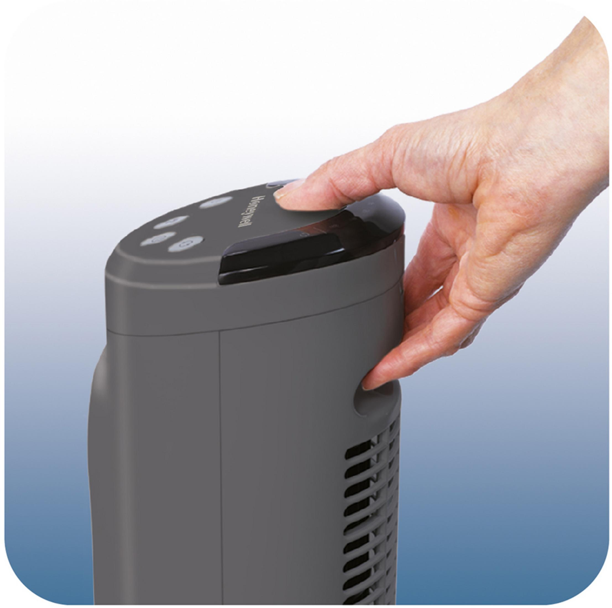 Ręka naciska przycisk na szarym wentylatorze, górna część widoczna na niebiesko-białym tle.