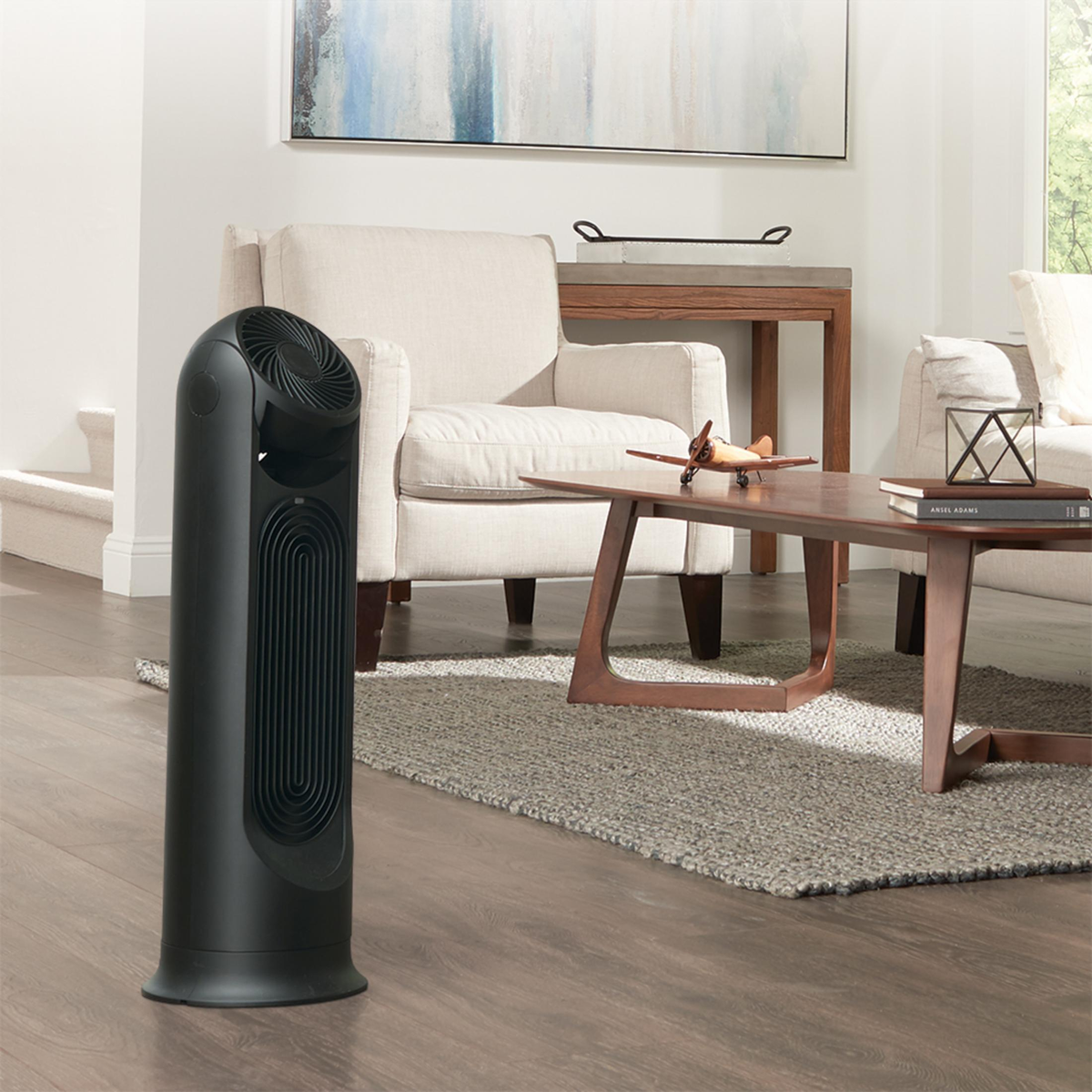 Czarny wentylator wieżowy w salonie, obok krzesła, stołu i dywanu.