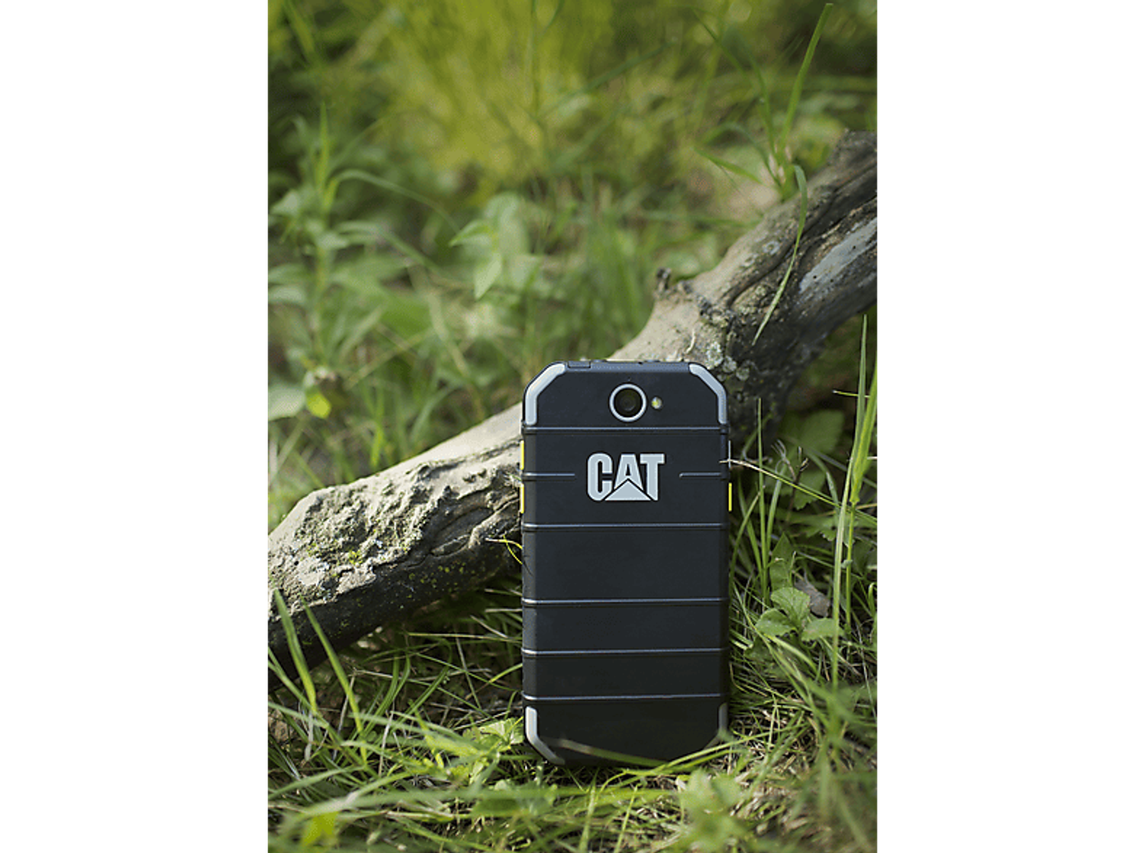 Schwarzes CAT-Telefon auf Gras mit einem Baumstamm. CAT-Logo sichtbar. Robustes Design.