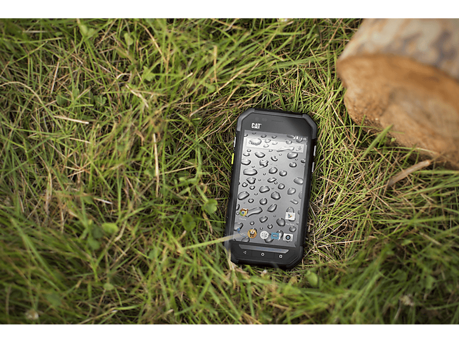 Ein robustes schwarzes Telefon mit Wassertropfen auf dem Bildschirm, das auf grünem Gras liegt.