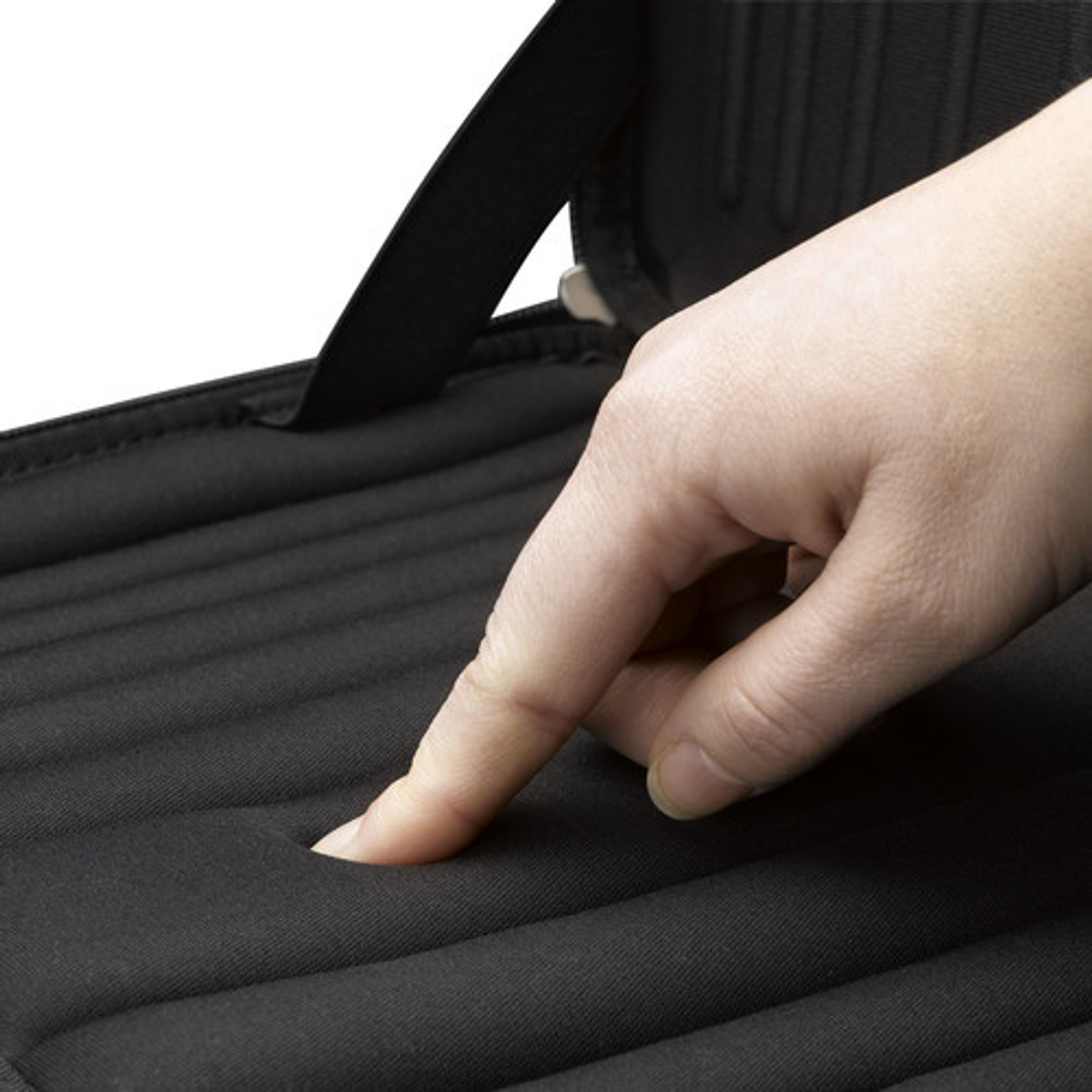 A finger pressing into a black, cushioned laptop surface, close-up on a light background.
