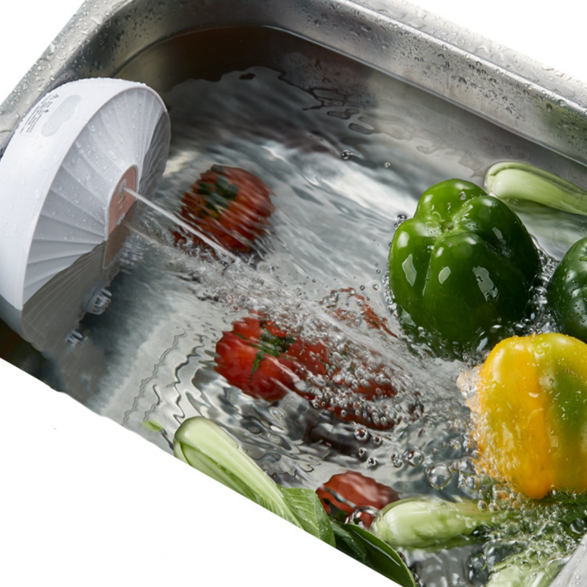Gemüse wird in einem Waschbecken gewaschen. Ein weißes Reinigungsgerät sprüht Wasser auf das Gemüse.