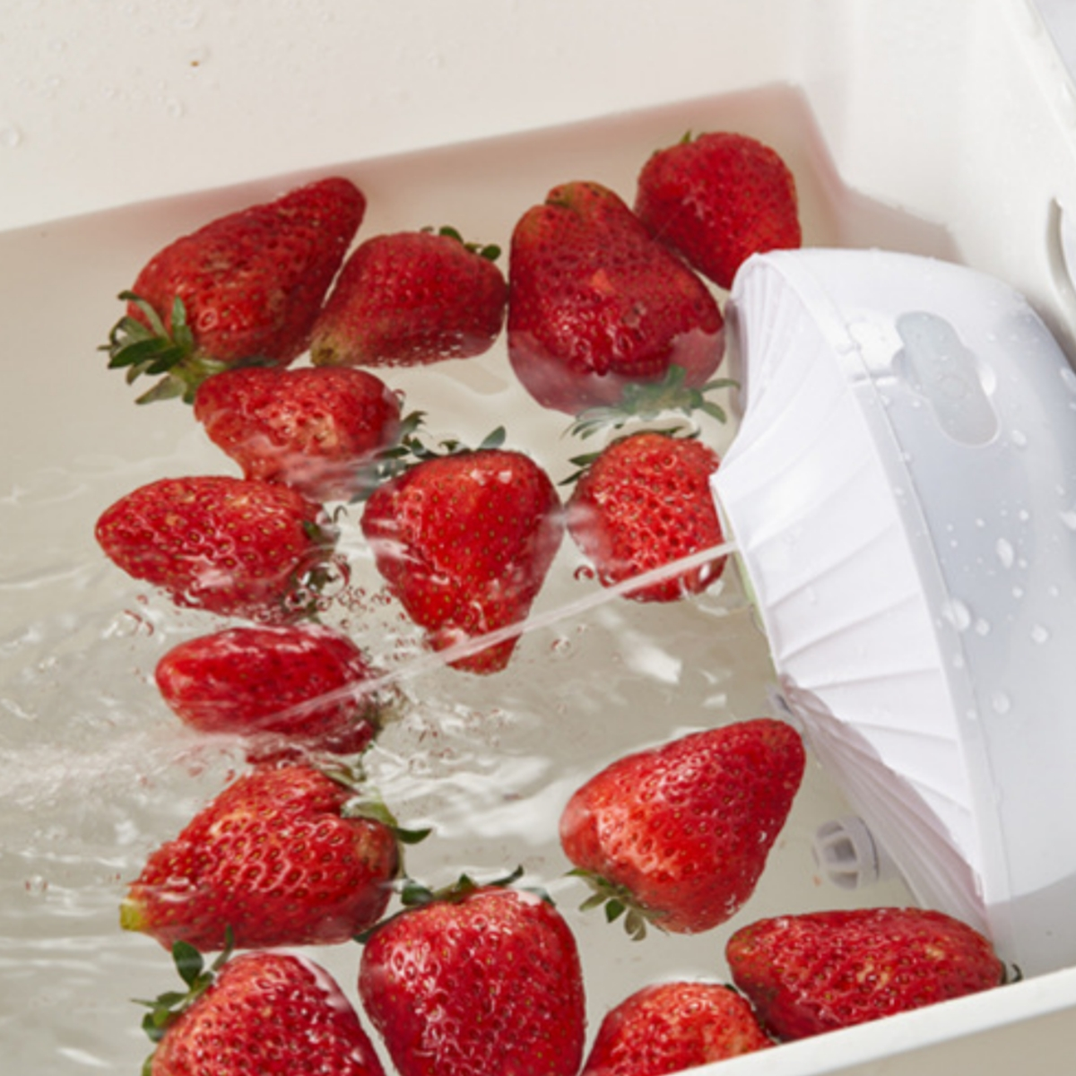 Nahaufnahme von frischen roten Erdbeeren, die in Wasser in einem weißen Behälter liegen.