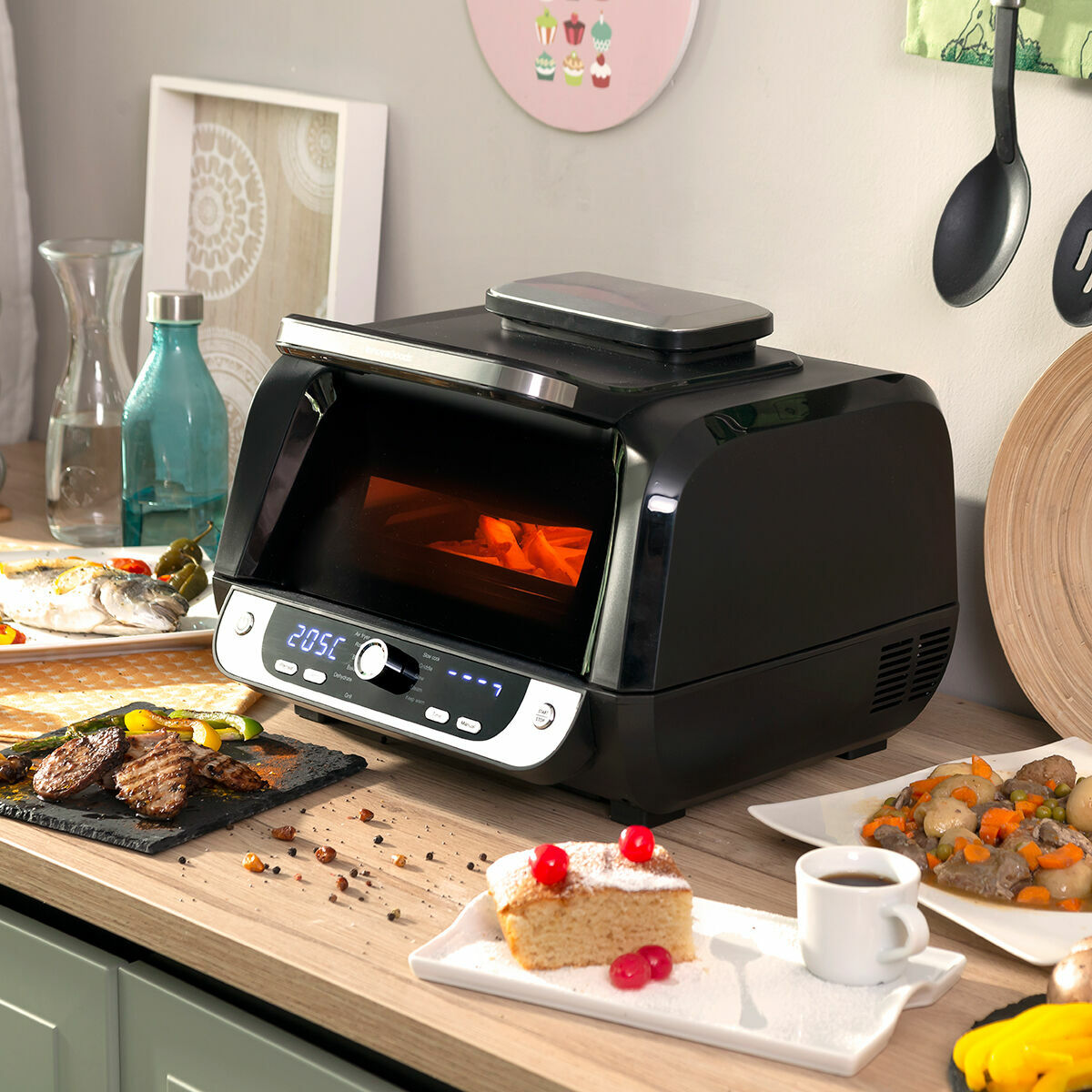 Forno nero su un bancone di legno con piatti di cibo e una torta. Il forno è acceso.