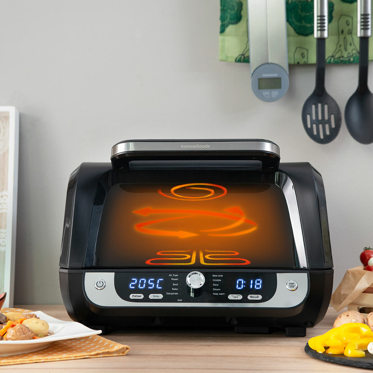 Friggitrice ad aria nera con display digitale che mostra 205C e 0:18. Cibo e utensili sullo sfondo.