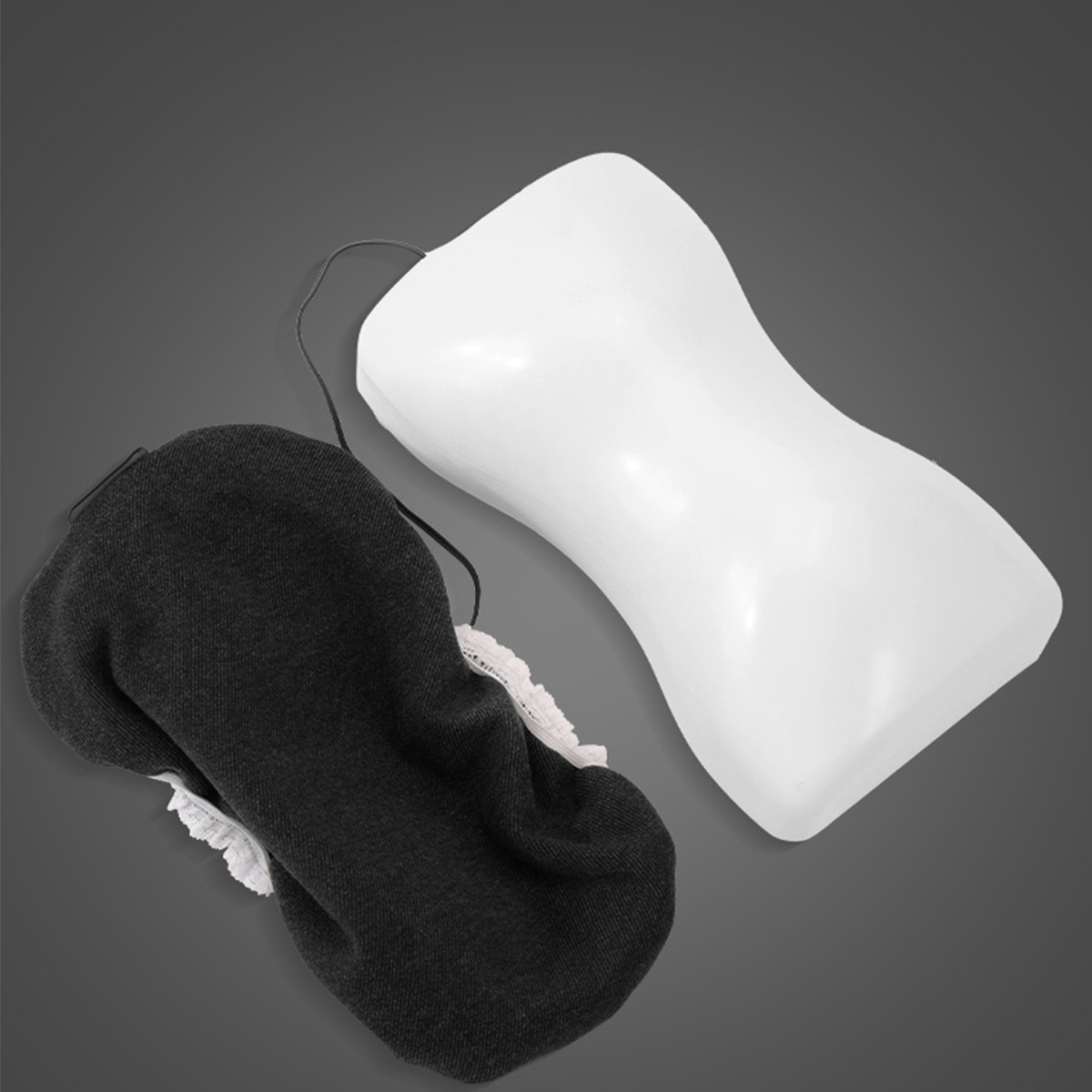 Schwarz-weiße Augenmaske und weißes Nackenkissen auf grauem Hintergrund.