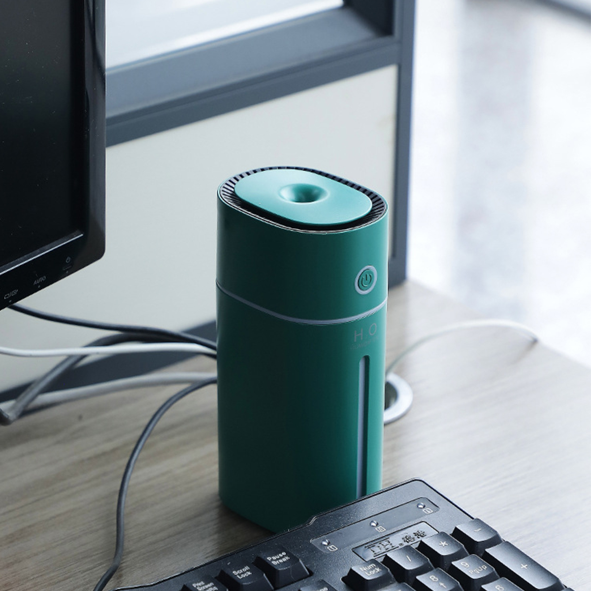 Grüner Luftbefeuchter auf einem Schreibtisch mit Tastatur und Computer im Hintergrund.