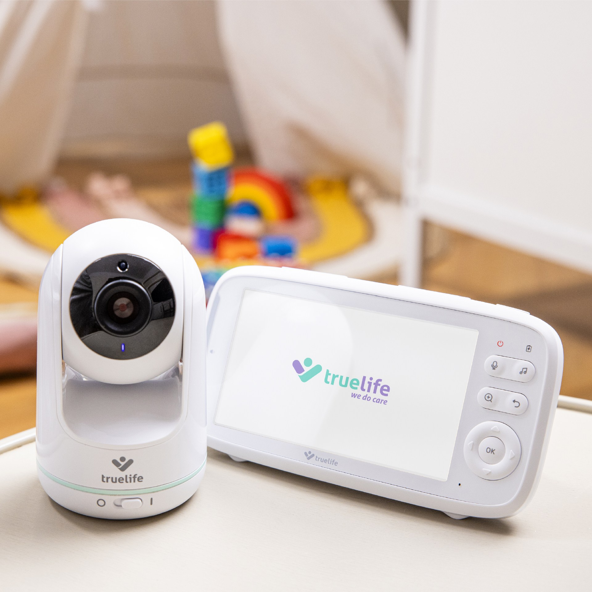 Babyphone-Kamera und Bildschirm. Der Bildschirm zeigt das Logo: truelife we do care. Spielzeug im Hintergrund.