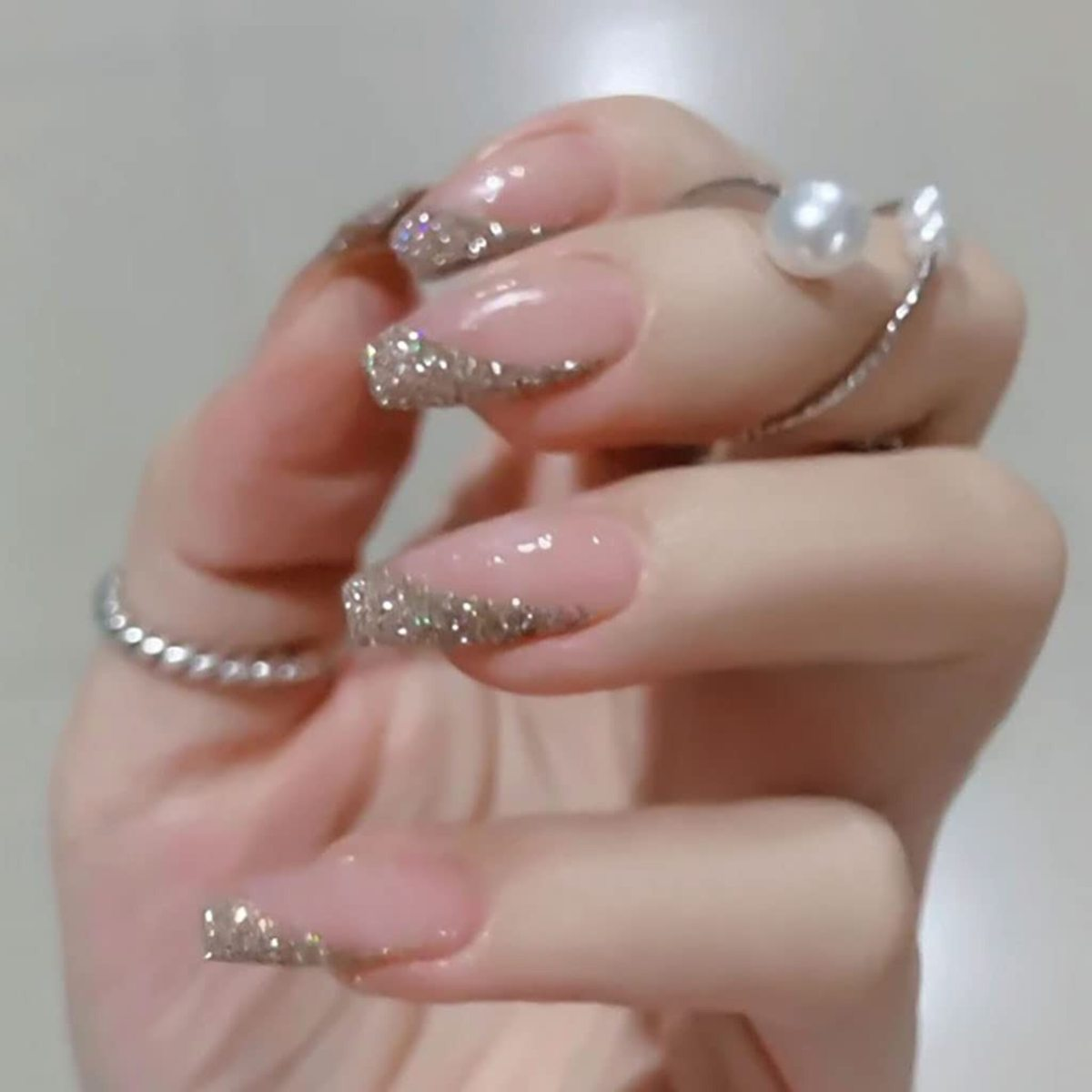 Nahaufnahme einer Hand mit elegantem, rosa Nagellack mit Glitzerakzenten und mehreren Ringen.