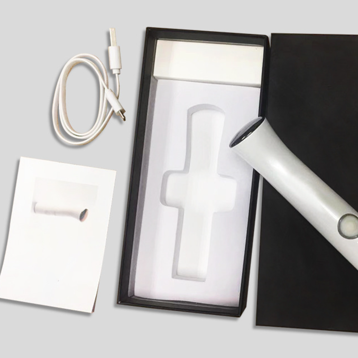 Weißes Schönheitsgerät und Ladekabel in schwarzer Box, mit weißem kreuzförmigem Einsatz.