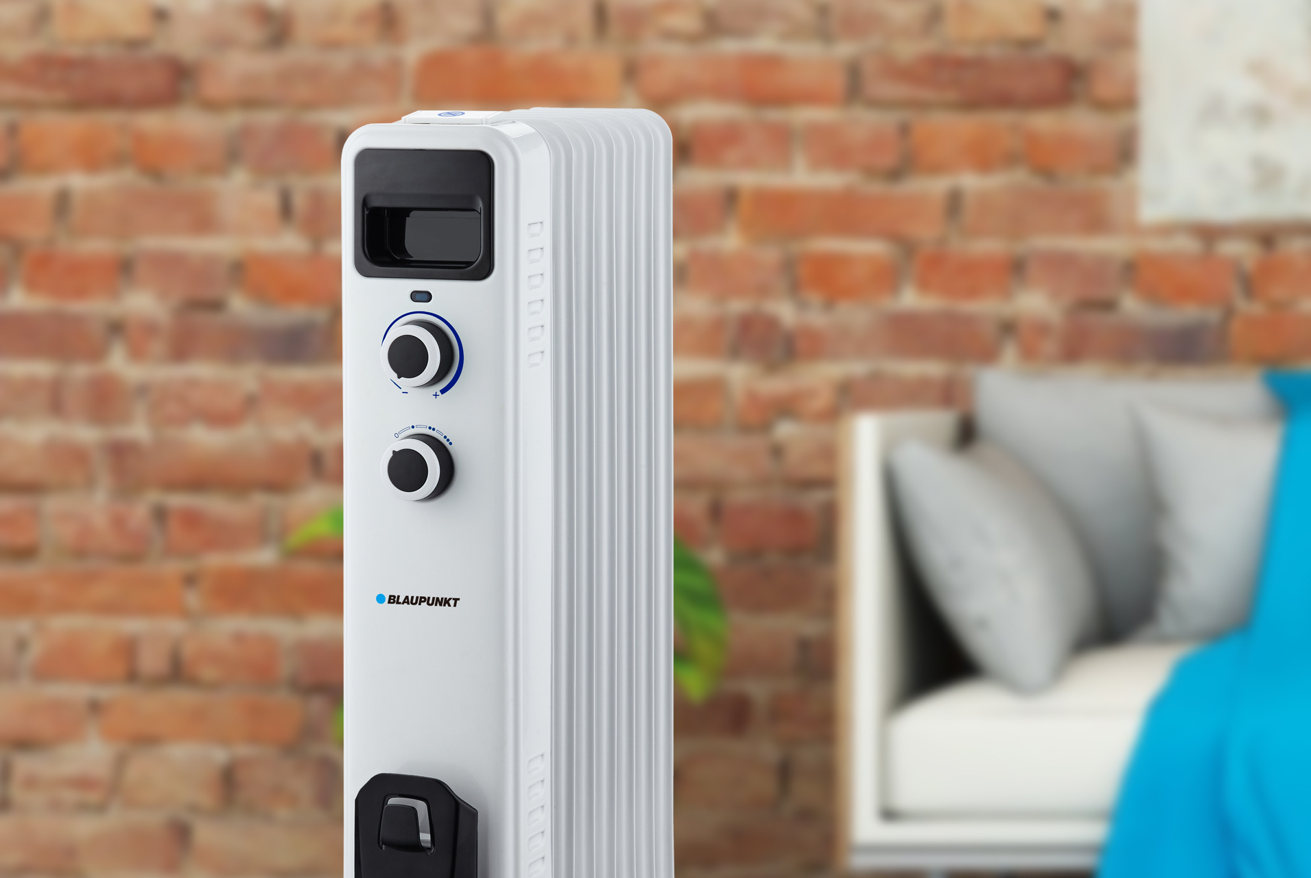 Biały grzejnik olejowy przed ceglaną ścianą i łóżkiem.