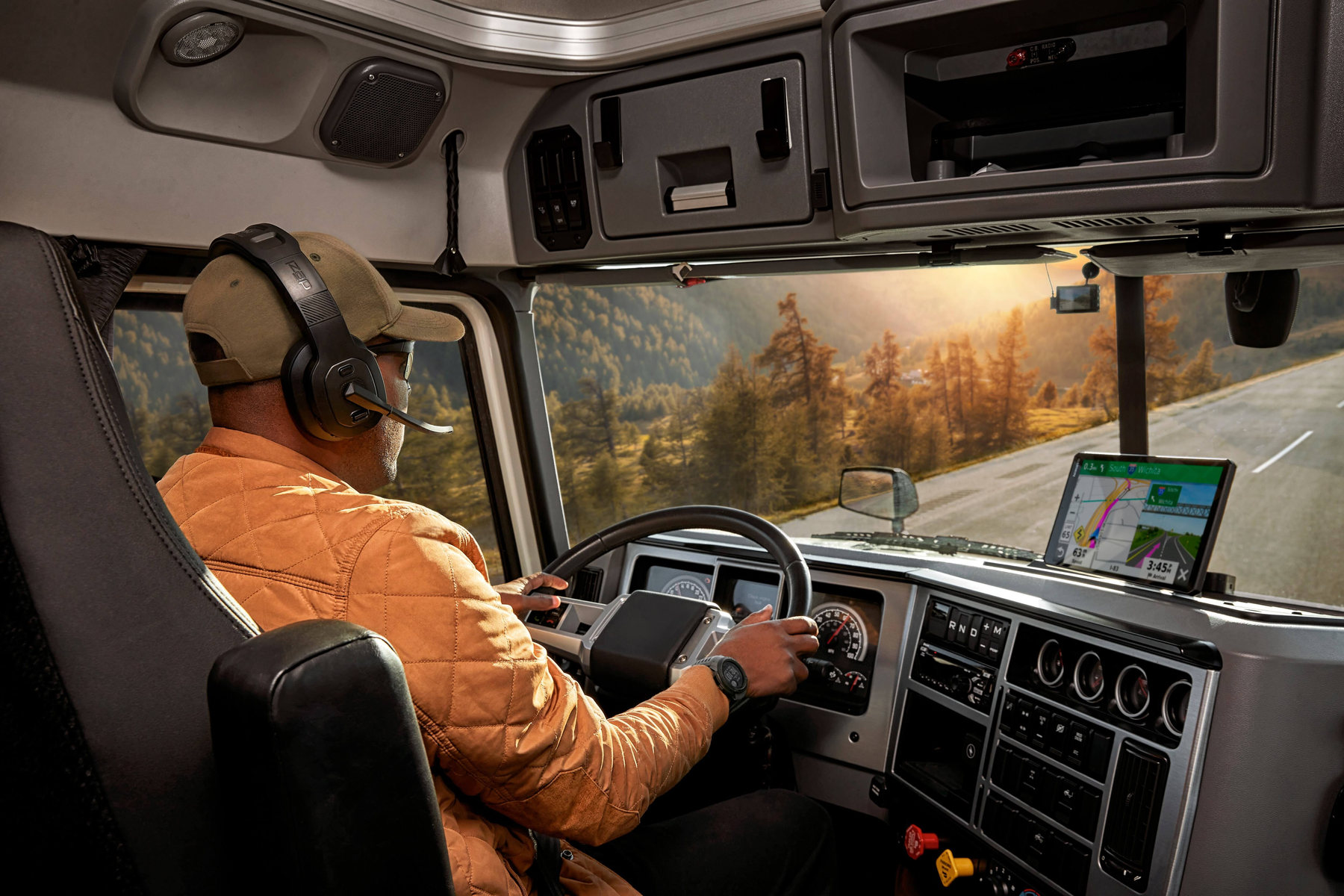 Ein Mann fährt LKW mit Headset, blickt auf GPS-Gerät am Armaturenbrett.