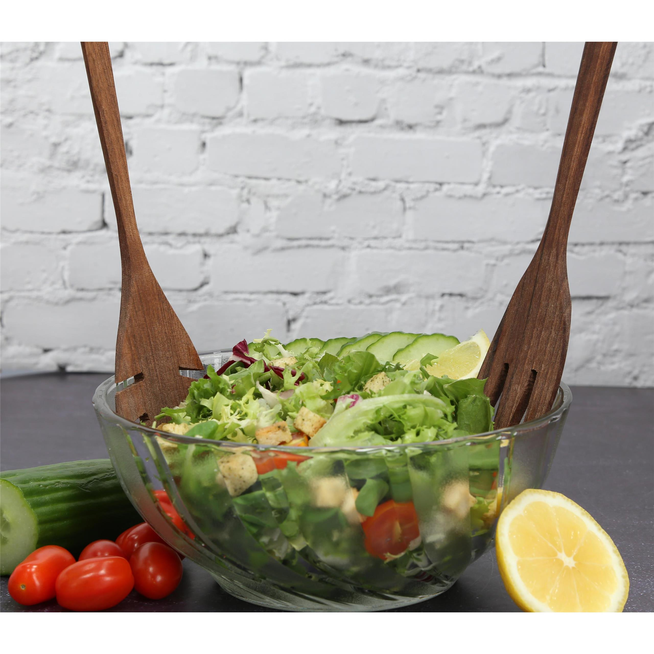 Eine Glasschüssel mit Salat und zwei Holzlöffeln. Eine Zitrone liegt daneben.