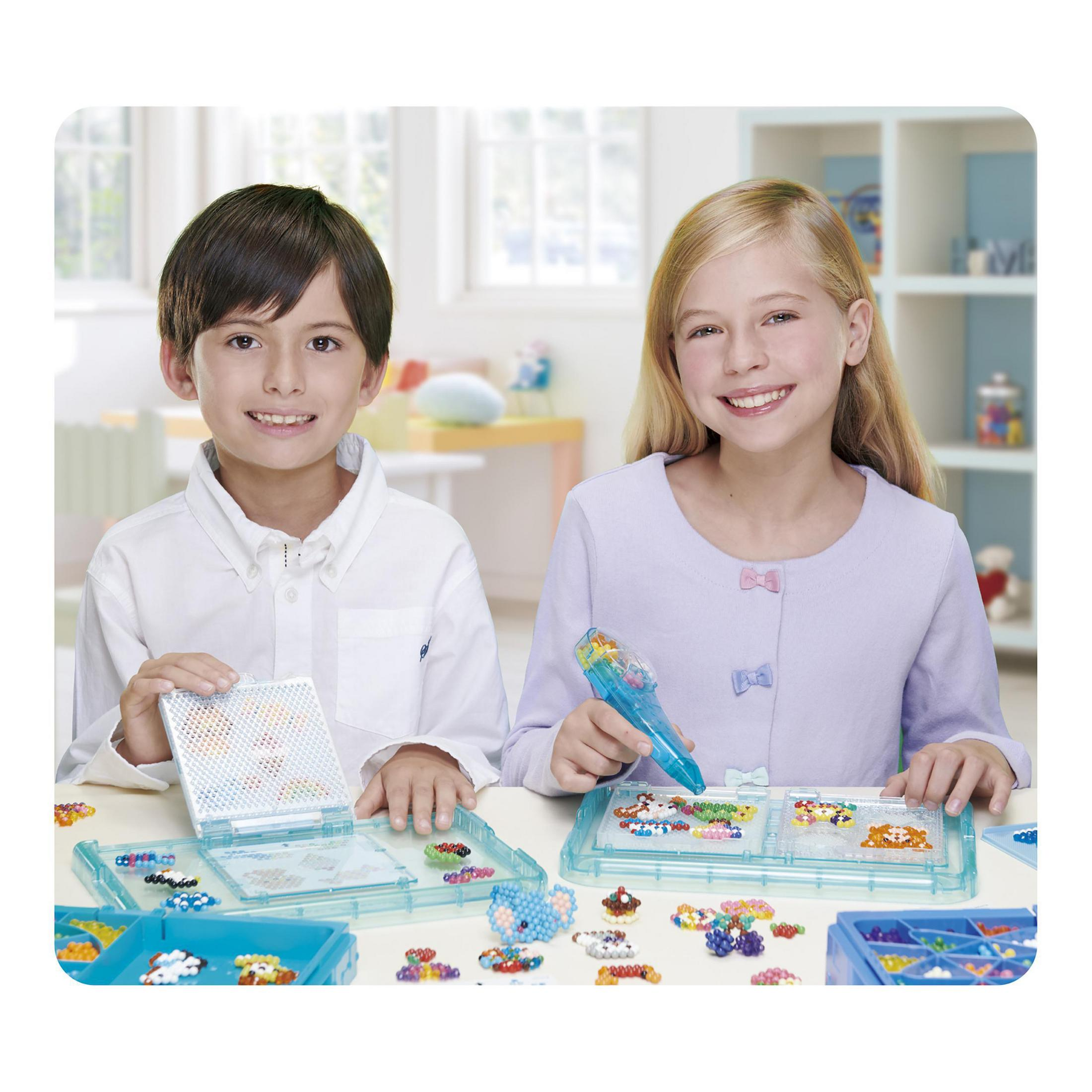 Due bambini sorridono alla fotocamera mentre giocano con perline colorate.