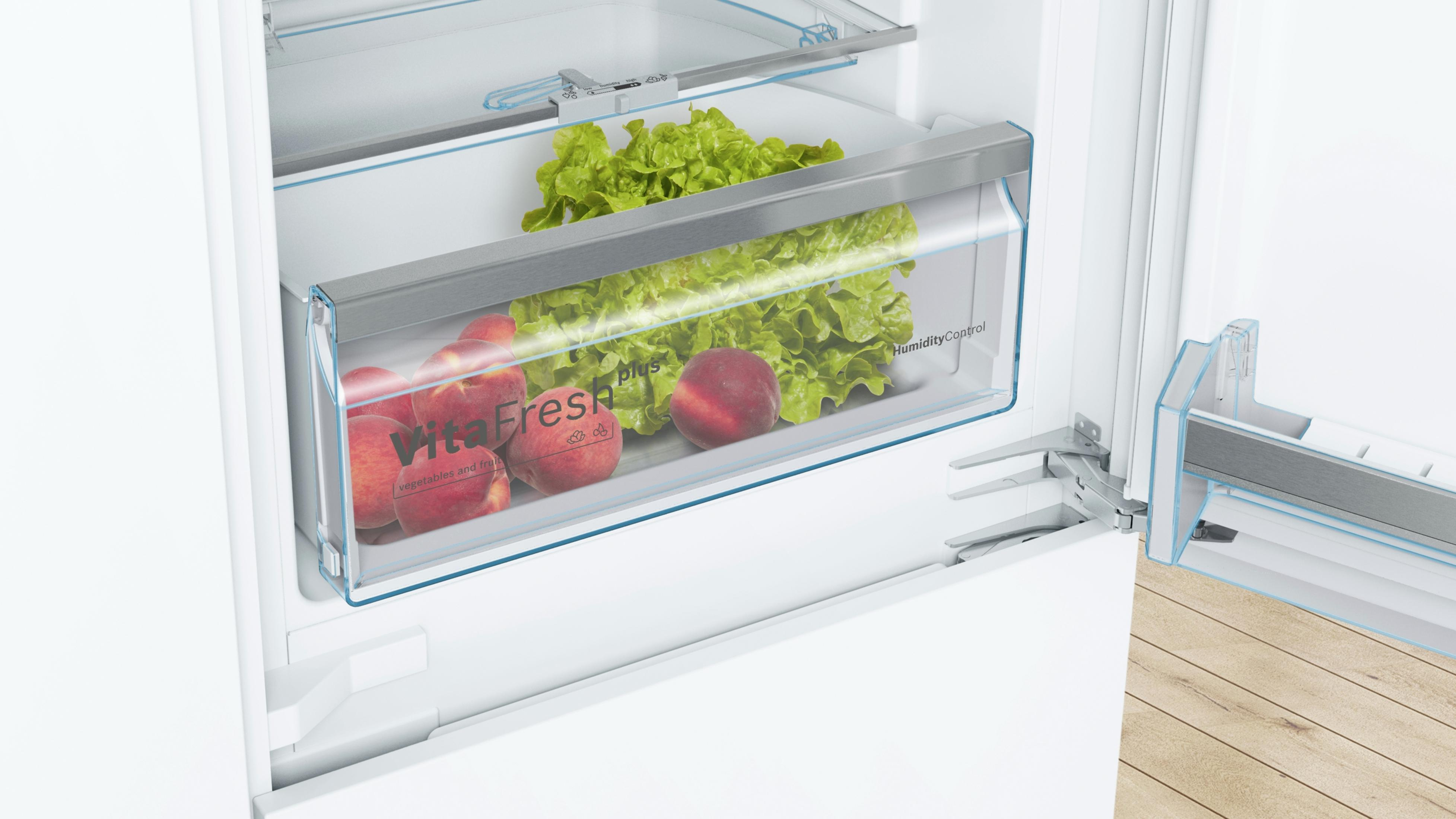 Kühlschrankinnenraum mit Schublade voller Salat und Pfirsiche, das VitaFresh plus-Etikett ist sichtbar.