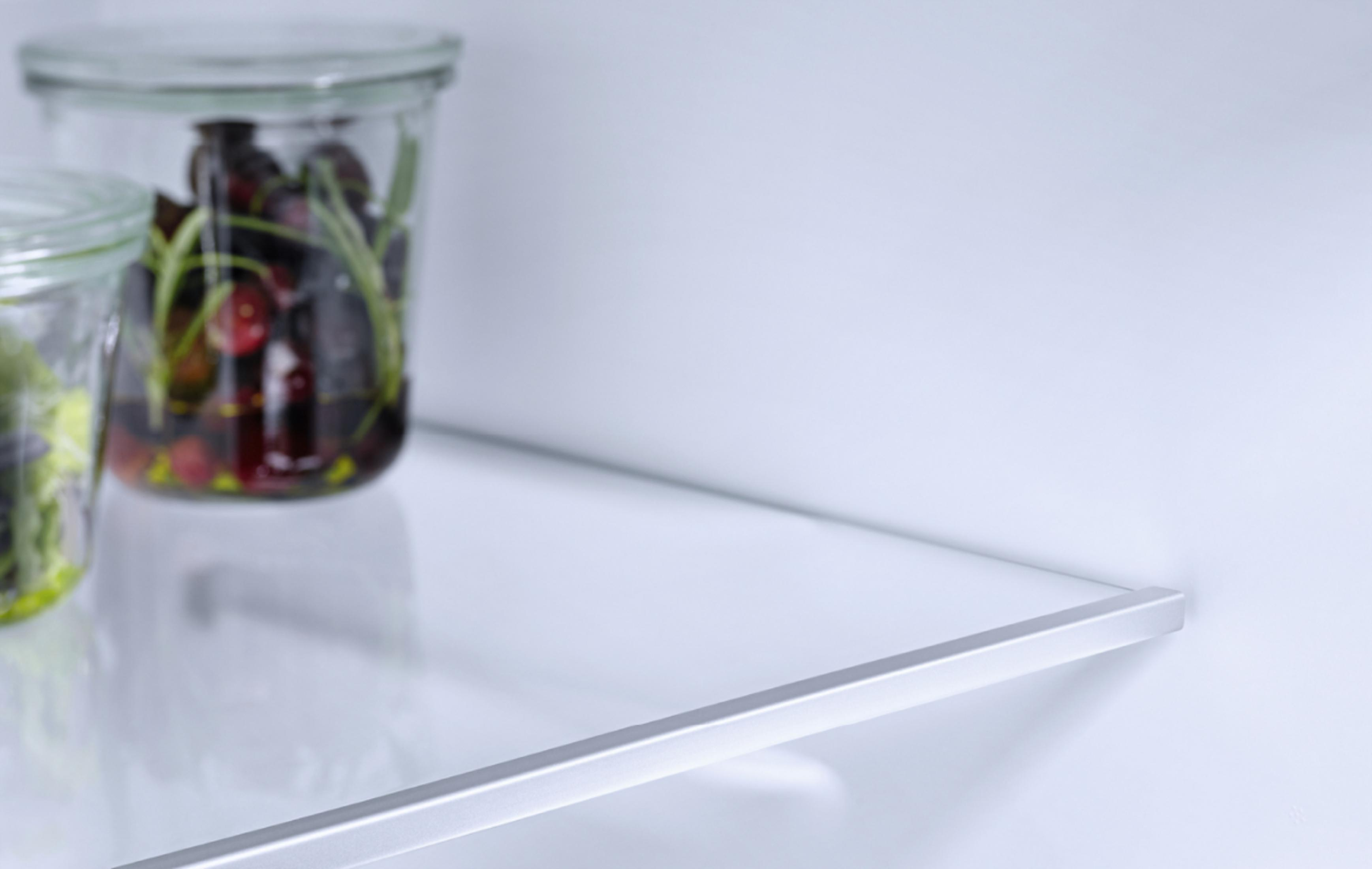 Eine Nahaufnahme eines transparenten Glasregals mit Gegenständen vor einer weißen Wand.