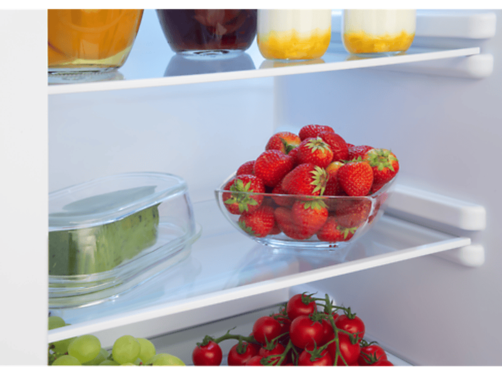 In einem Kühlschrank: Erdbeeren in einer Schüssel, Gläser und andere Lebensmittel.