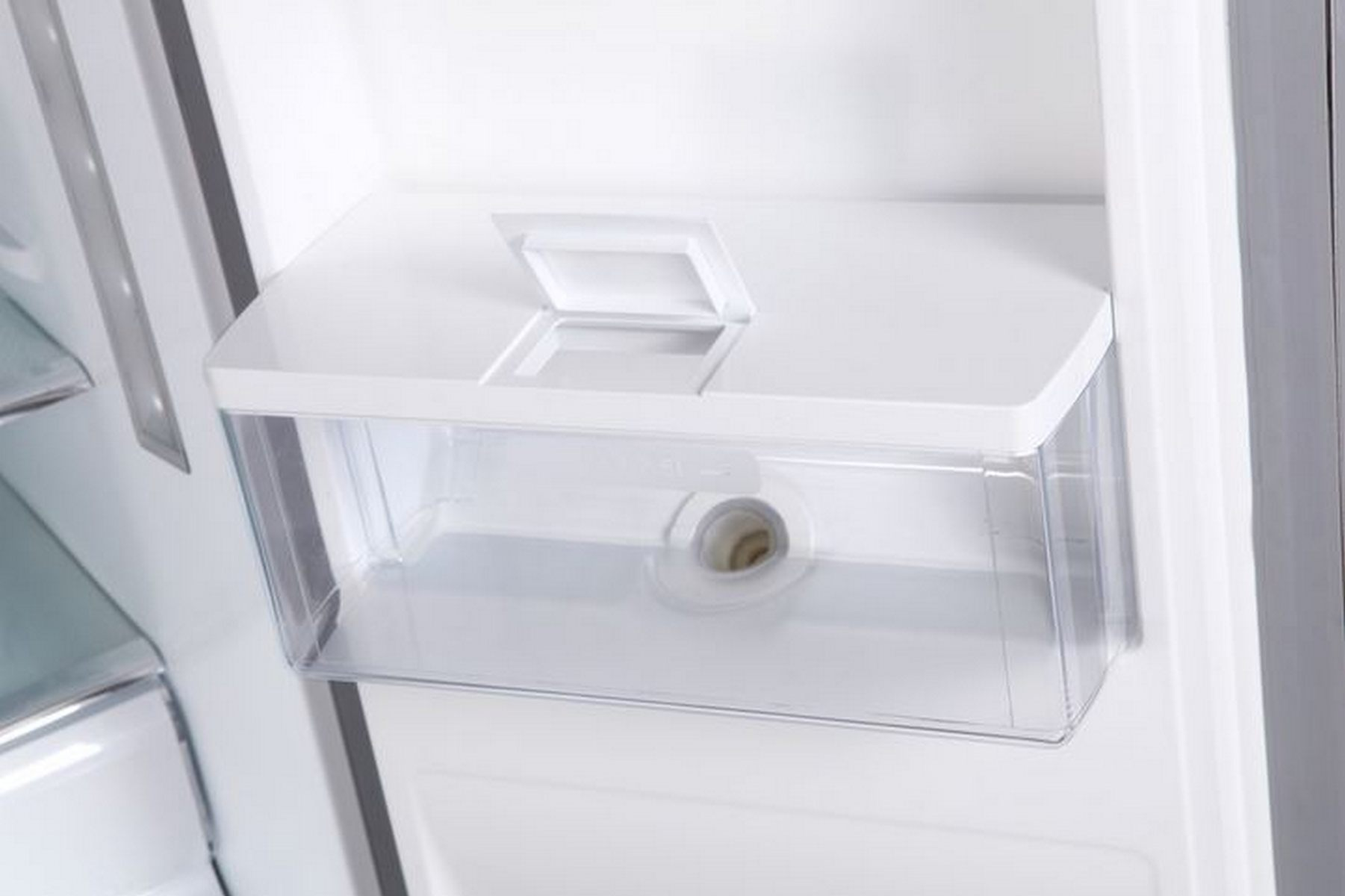 Dentro de una nevera: un contenedor de hielo blanco con tapa y un recipiente de plástico transparente.