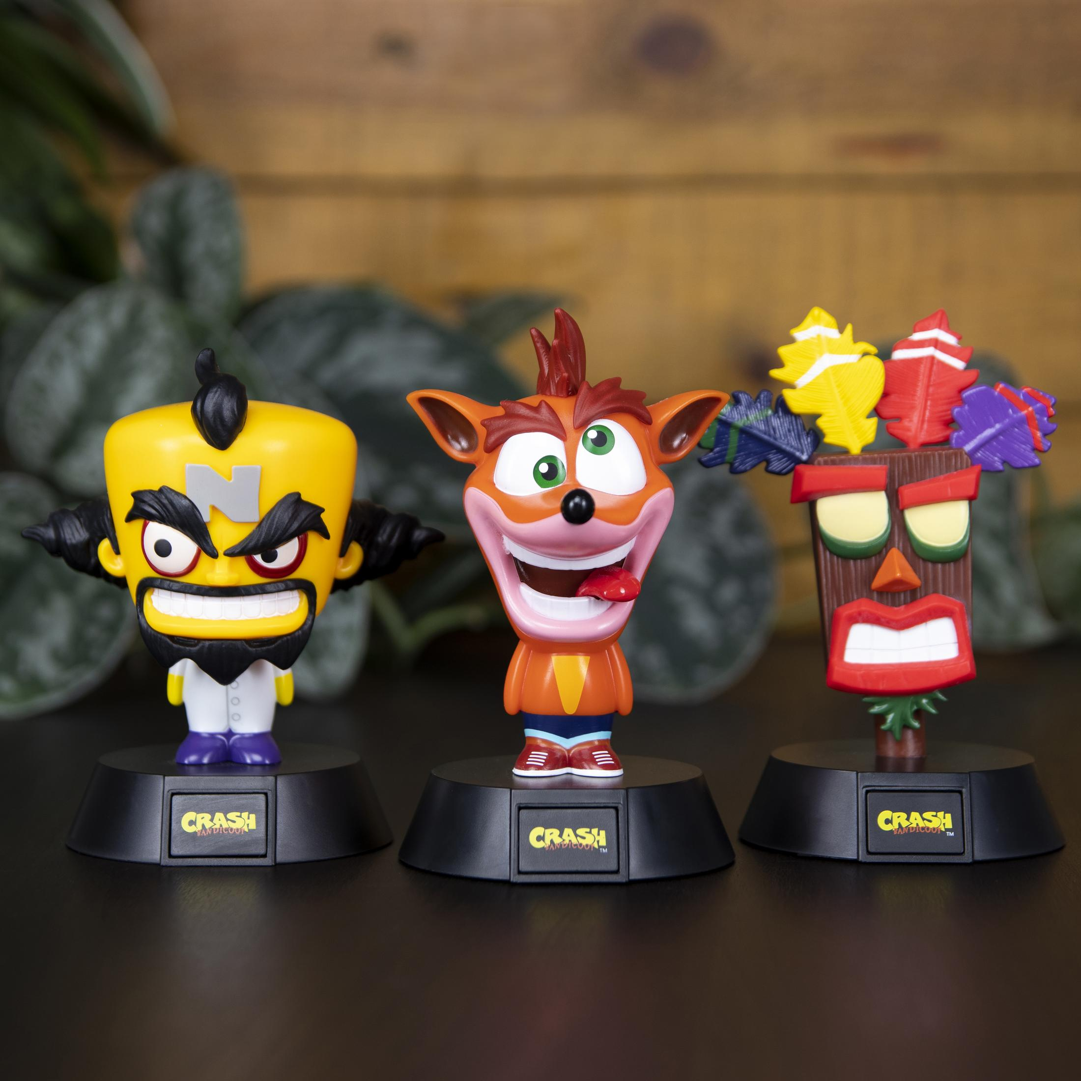 Drei Crash Bandicoot Figuren: Cortex, Crash und eine Tiki-Maske, auf schwarzen Sockeln, Holz Hintergrund.