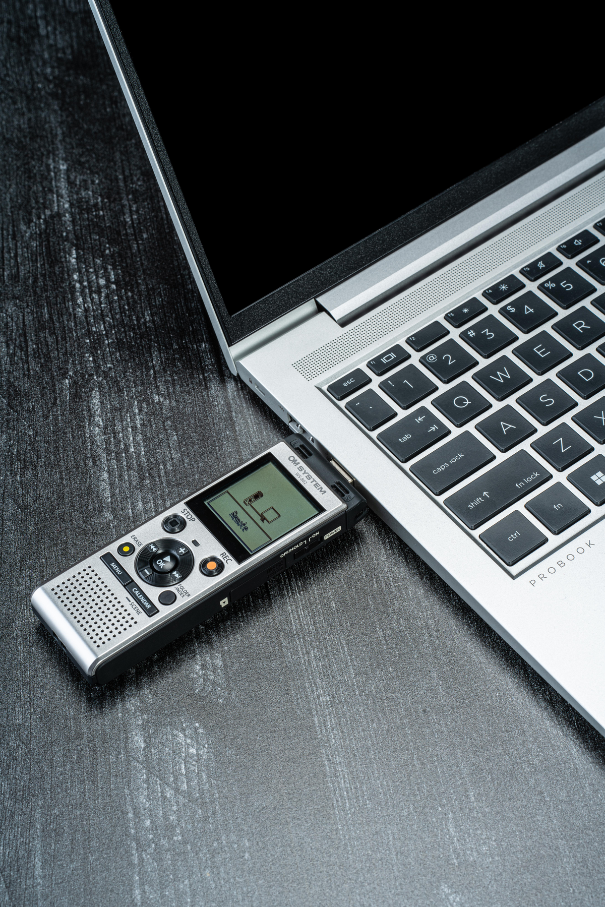 Cyfrowy rejestrator podłączony do laptopa, na ciemnej powierzchni z fakturą drewna.