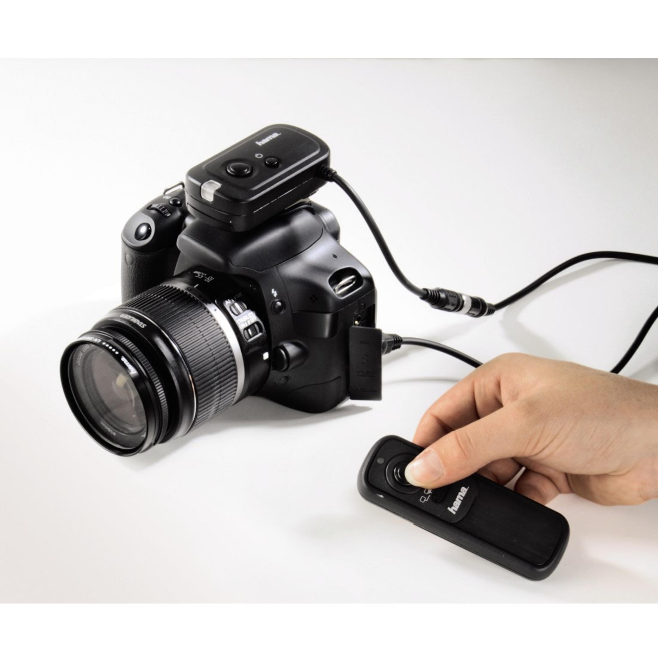 Eine schwarze DSLR-Kamera mit Fernbedienung und einer Hand, die eine zweite Fernbedienung hält.