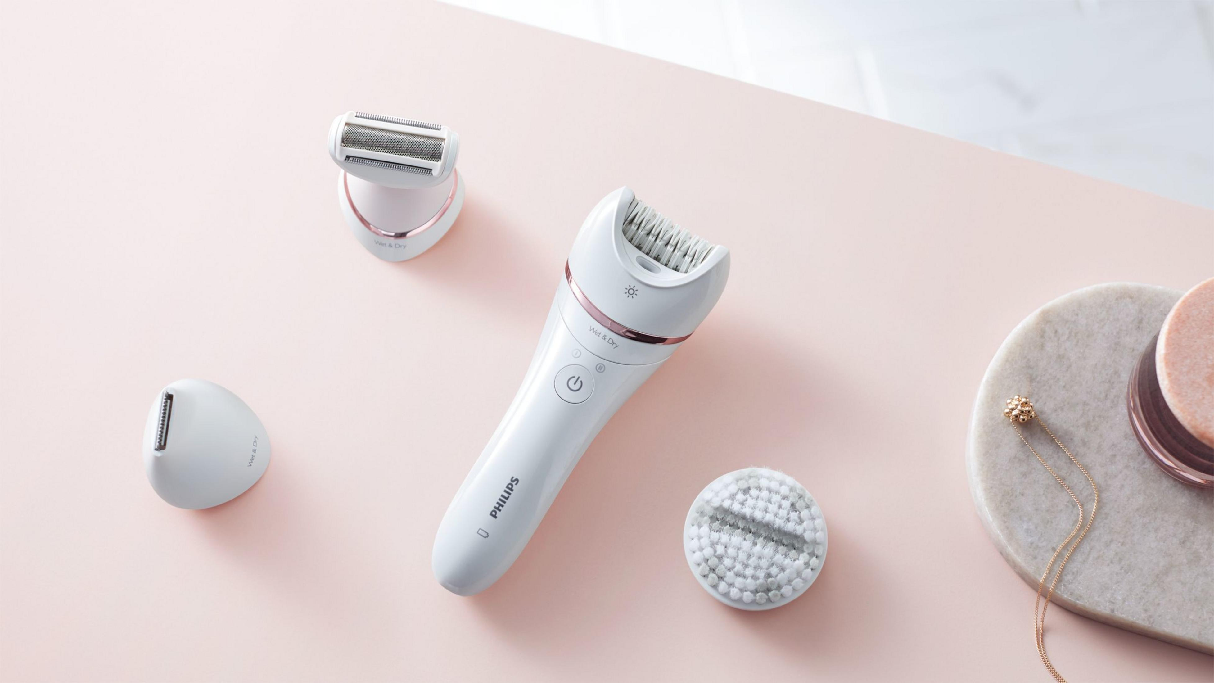Weiße Elektrorasierer und Zubehör auf rosa Oberfläche. Enthält Rasierer, Trimmer und Bürste.