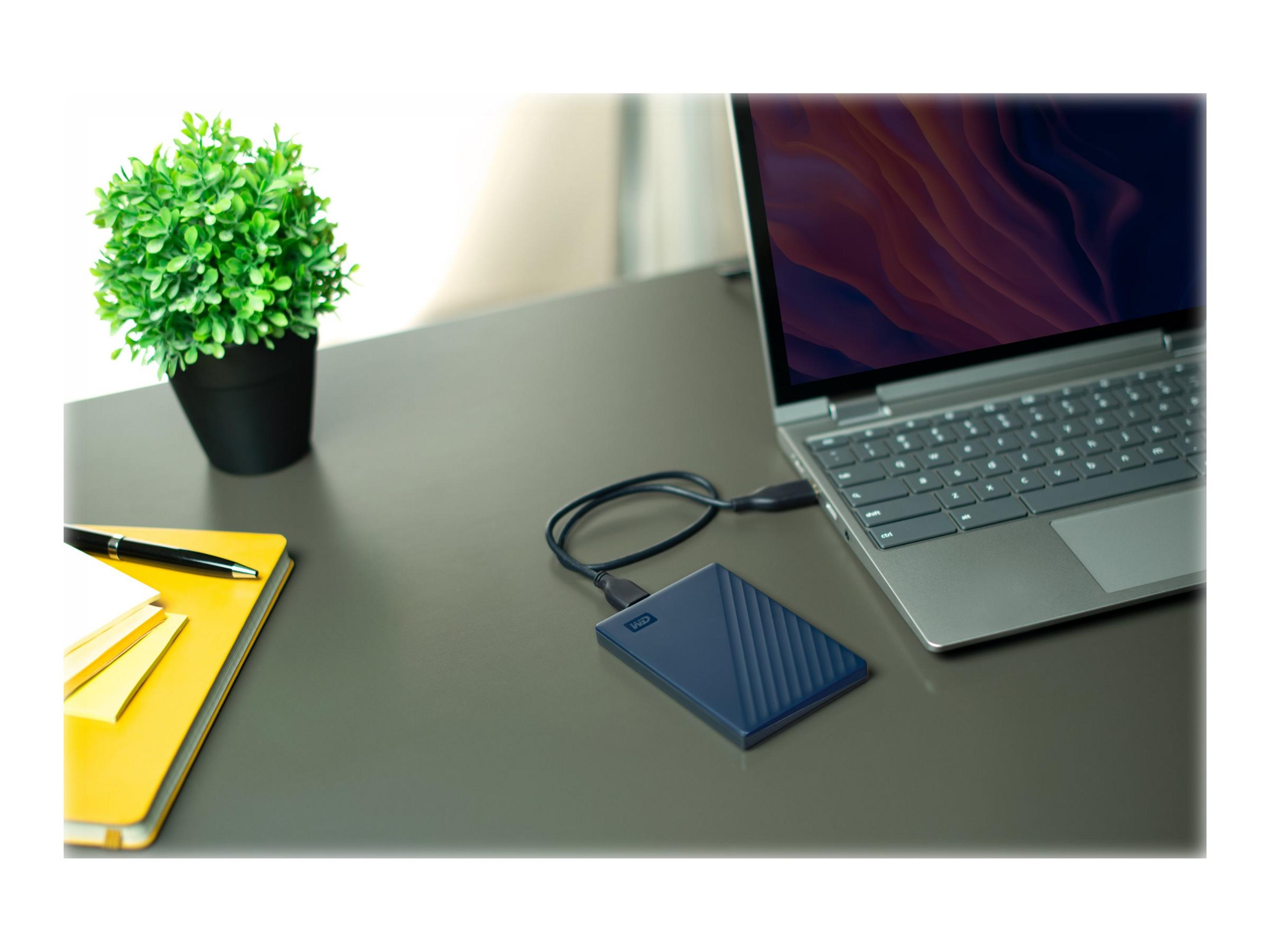 Laptop otwarty obok przenośnego dysku twardego i rośliny na szarym biurku.