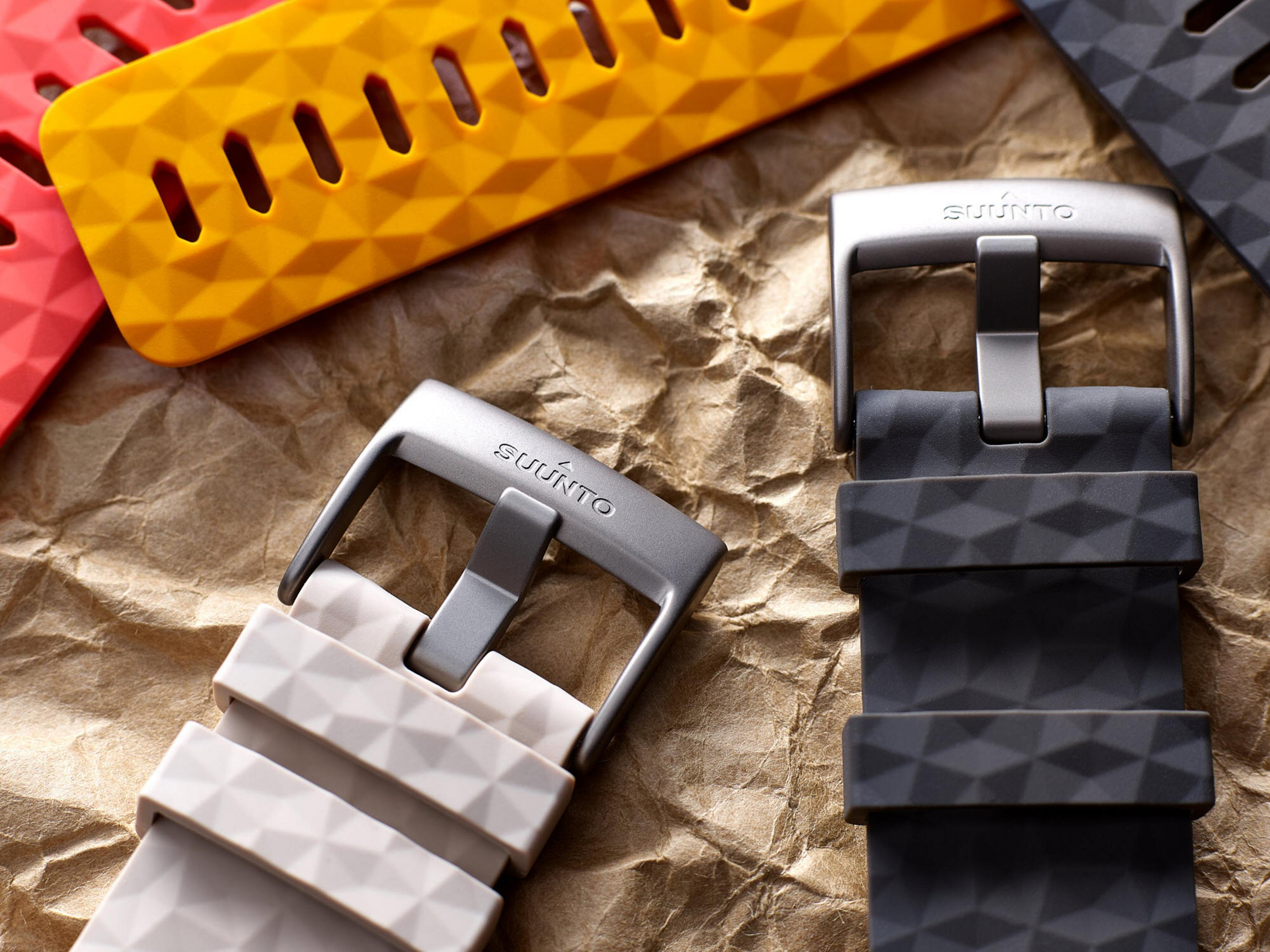 Zbliżenie pasków do zegarków w kolorze szarym, żółtym i czerwonym, z marką Suunto na teksturowanej powierzchni.