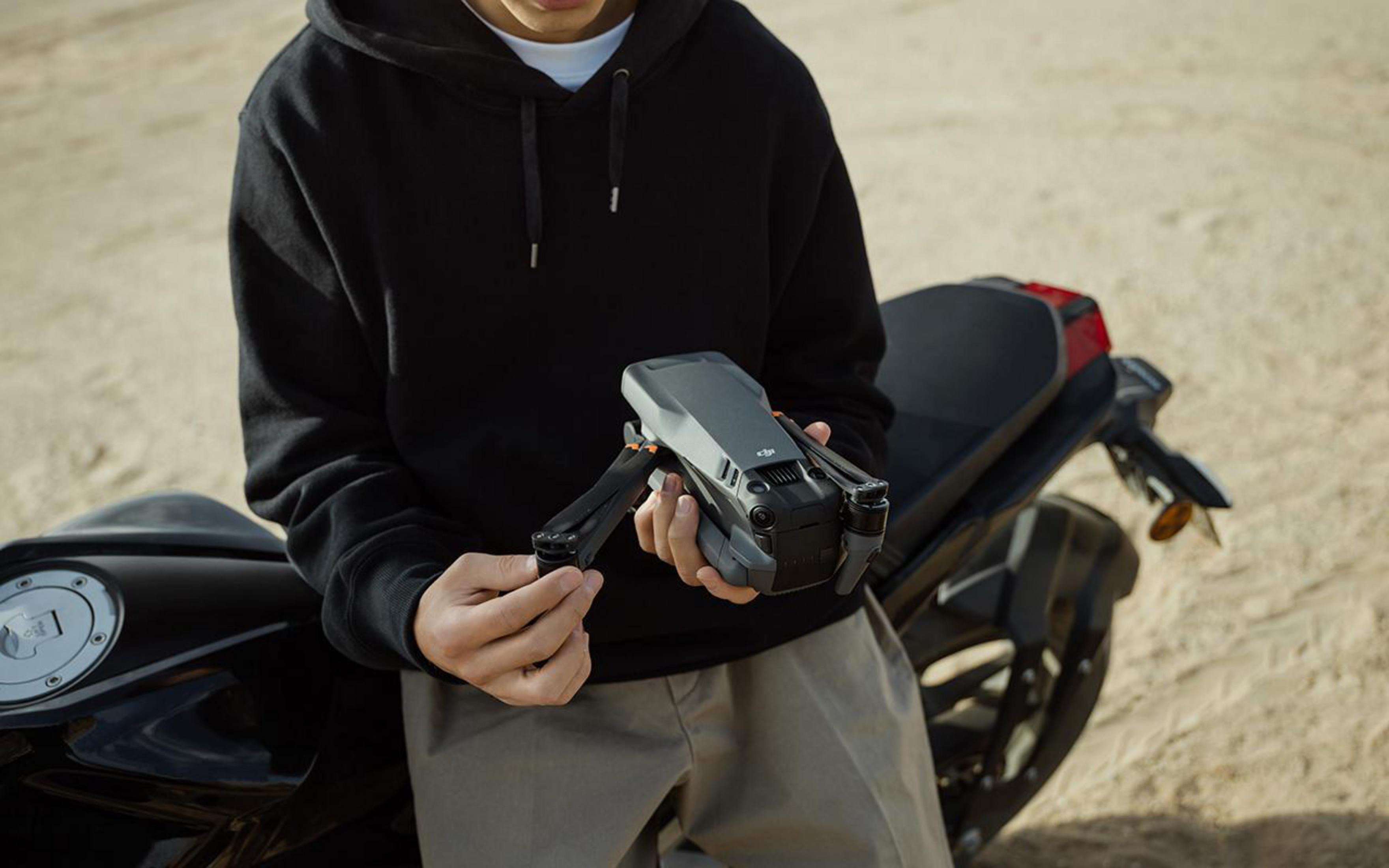 Person hält eine Drohne. Motorrad im Hintergrund. Umgebung im Freien.