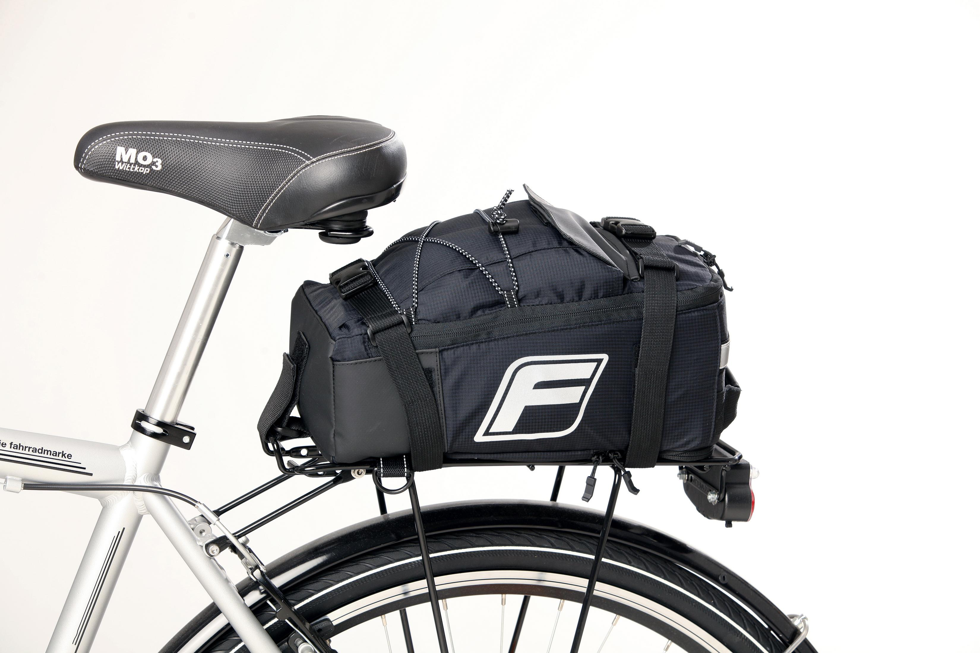 Una bicicleta negra con una bolsa negra montada en el portaequipajes trasero. La bolsa tiene un logo blanco.