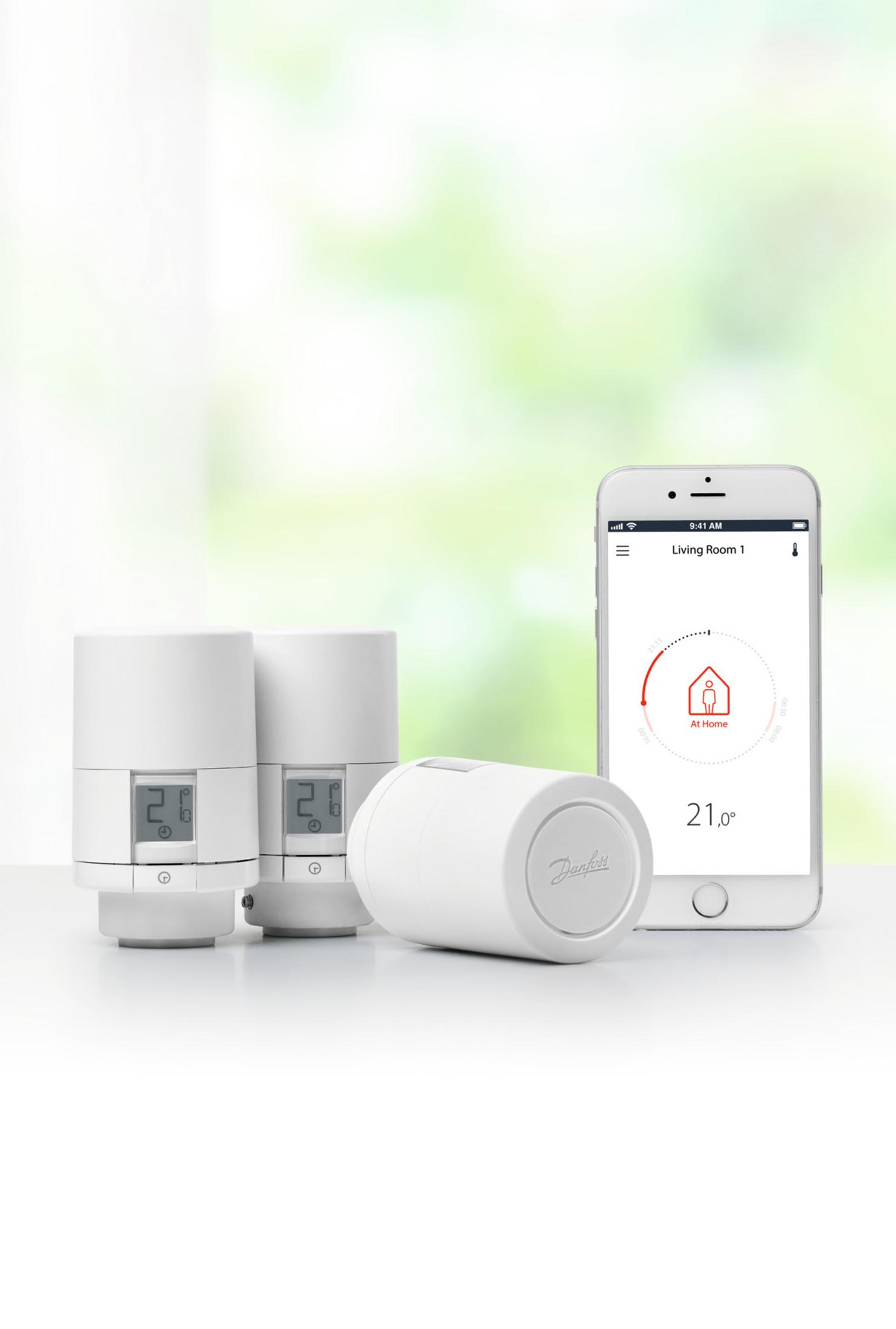 Weiße intelligente Thermostatgeräte und ein Smartphone. Das Telefon zeigt eine Temperatur von 21° an.