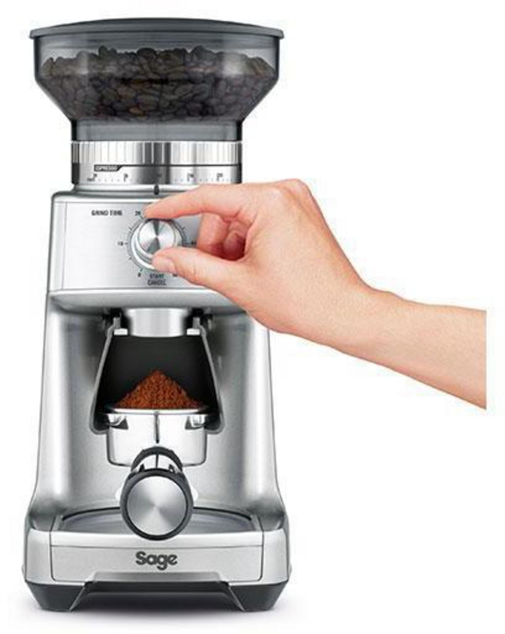 Una mano gira el dial de tamaño de molienda en un molinillo de café plateado con granos de café.
