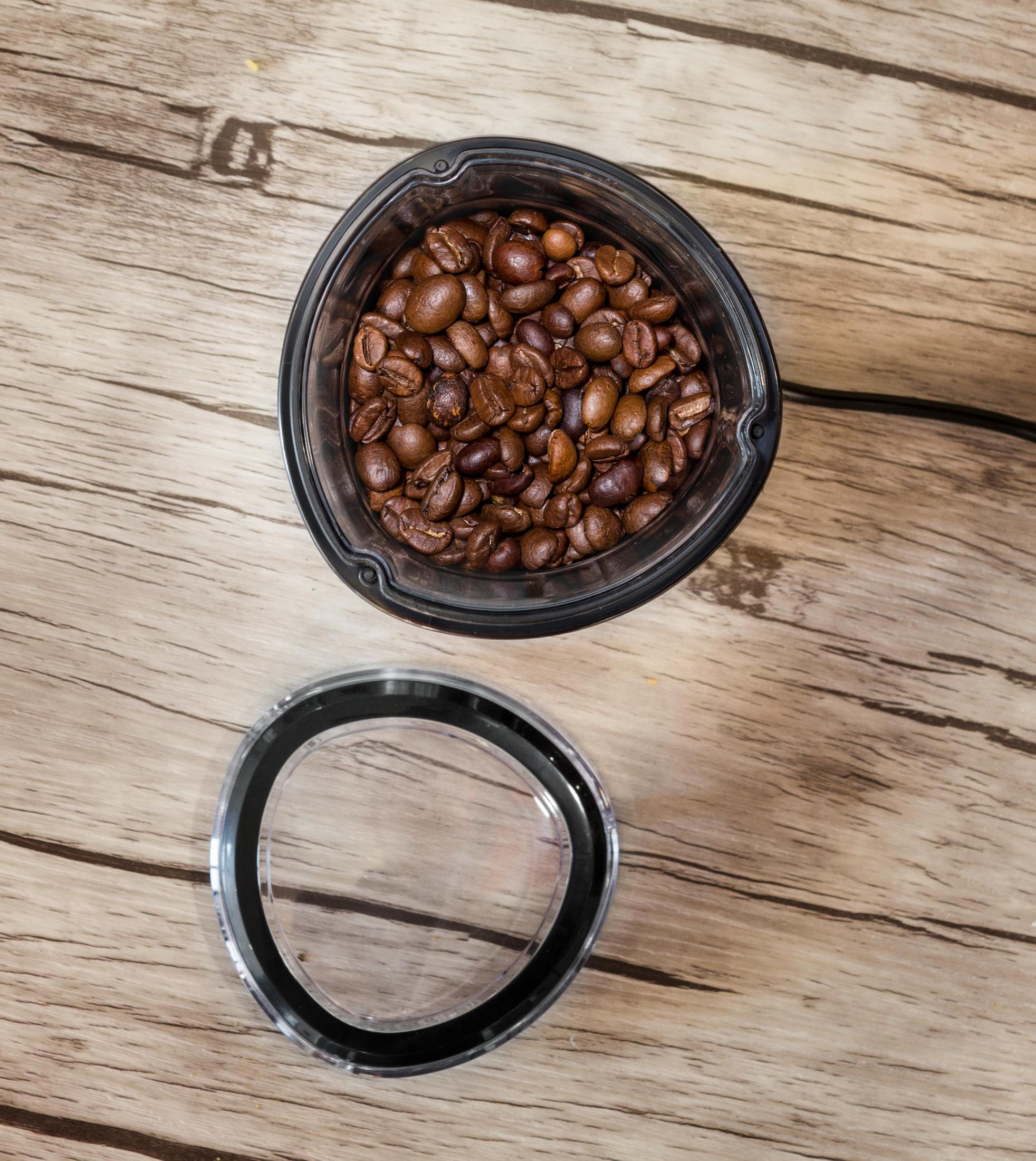 Młynek do kawy z ziarnami kawy w środku, otwarte wieczko obok na drewnianej powierzchni.