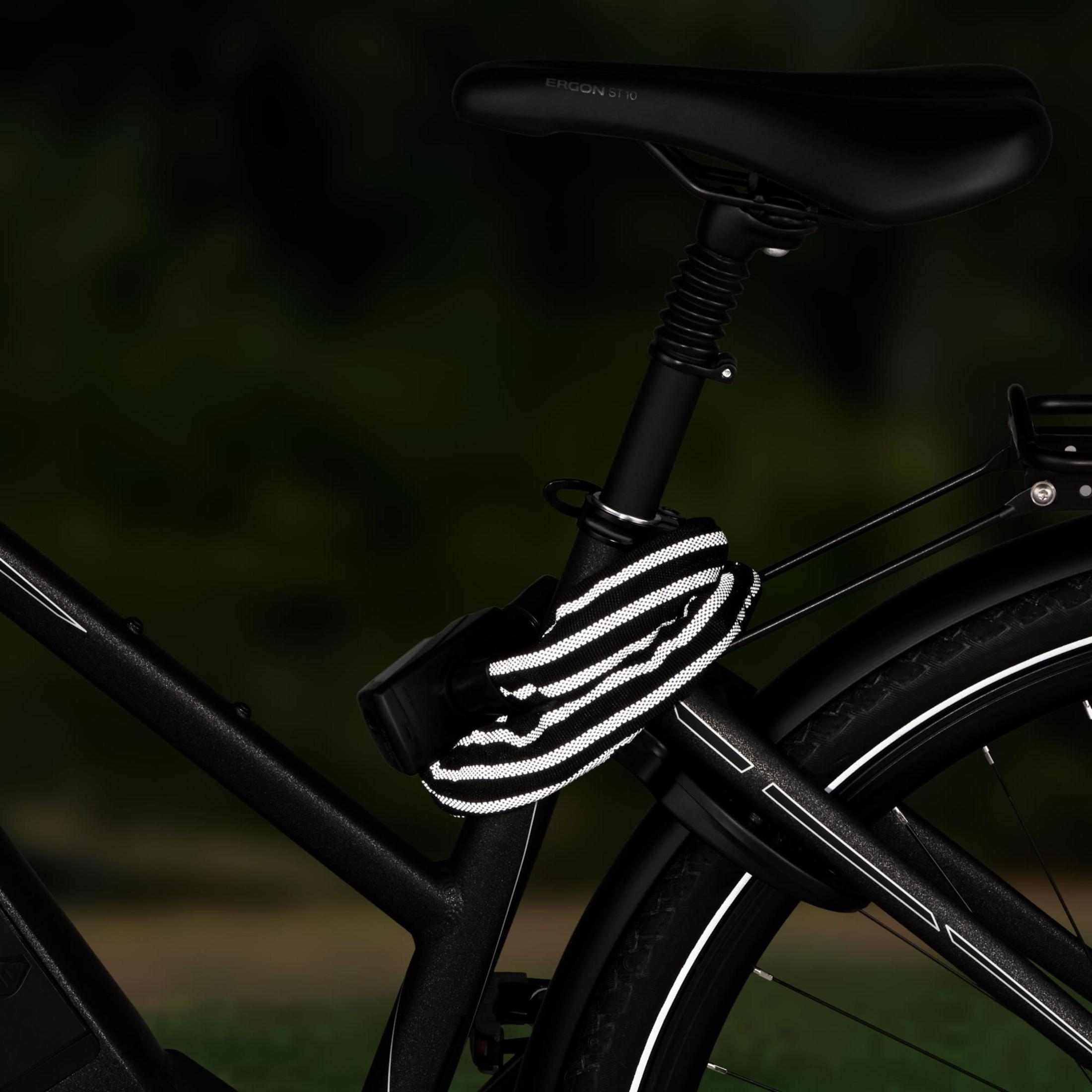 Primo piano di una bicicletta nera con un lucchetto riflettente attaccato al telaio. Sfondo scuro.