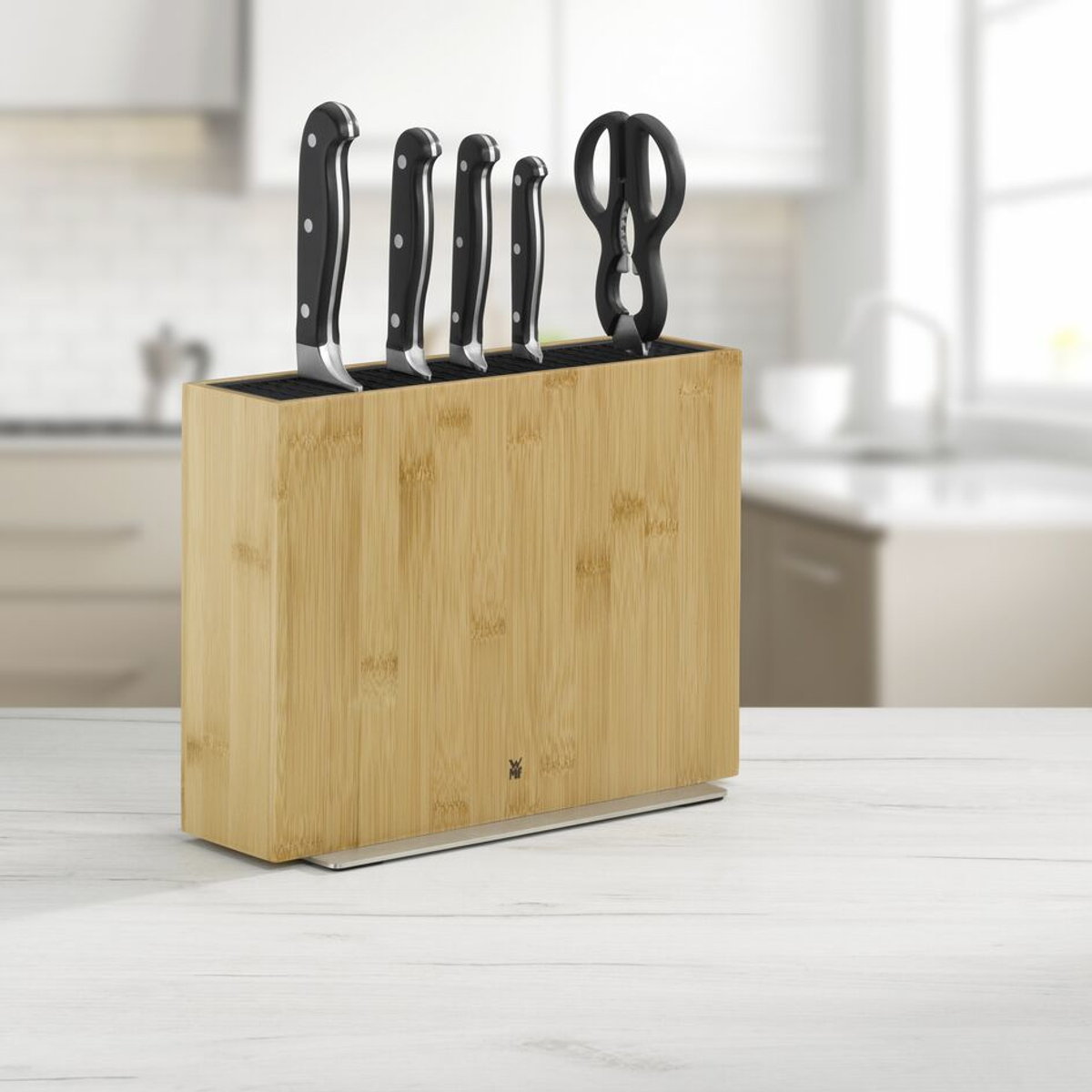 Bloc de couteaux avec couteaux et ciseaux sur une surface blanche, cuisine en arrière-plan.