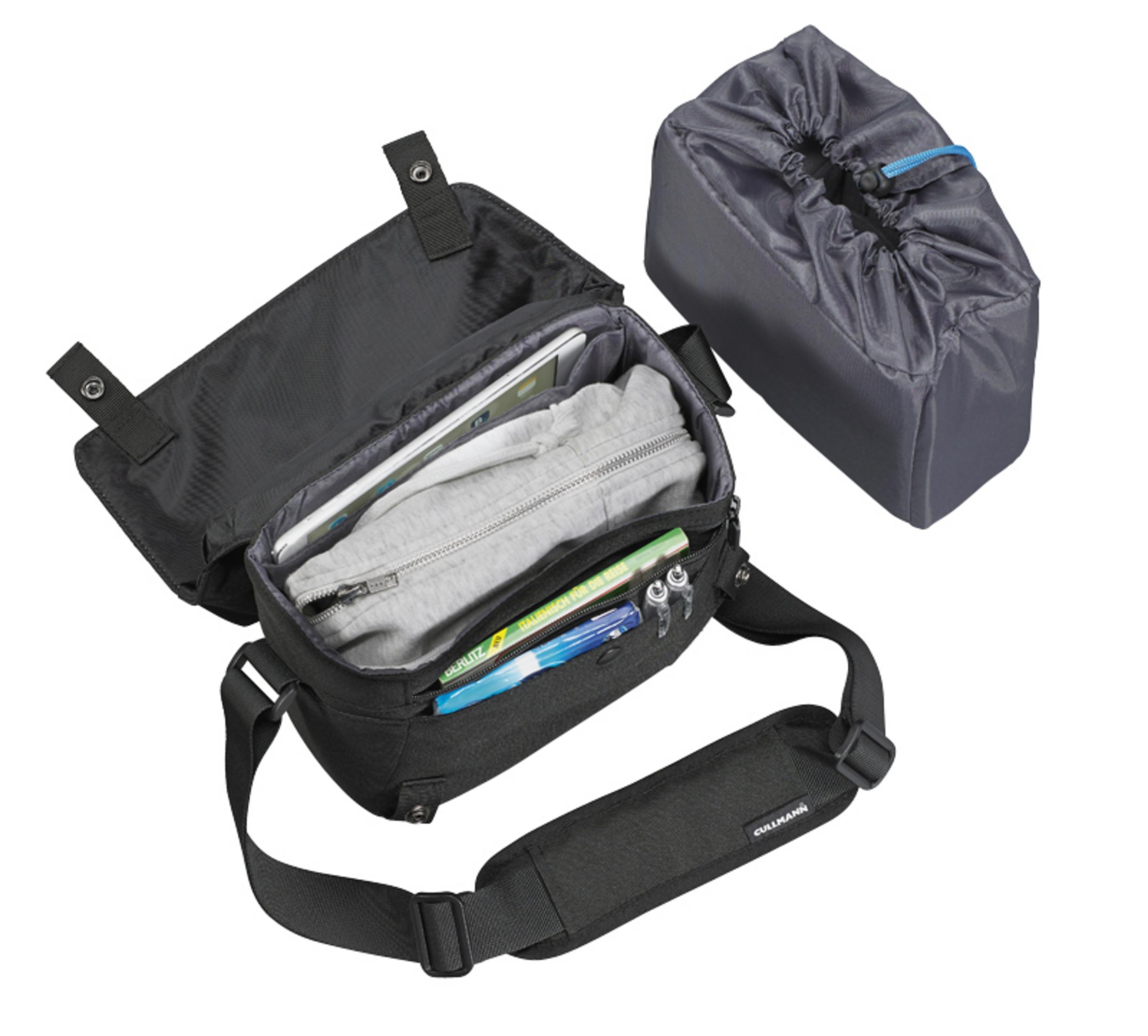 Schwarze Kameratasche mit Inhalt: Tablet, Pullover, Stifte und Notizbuch, weißer Hintergrund.