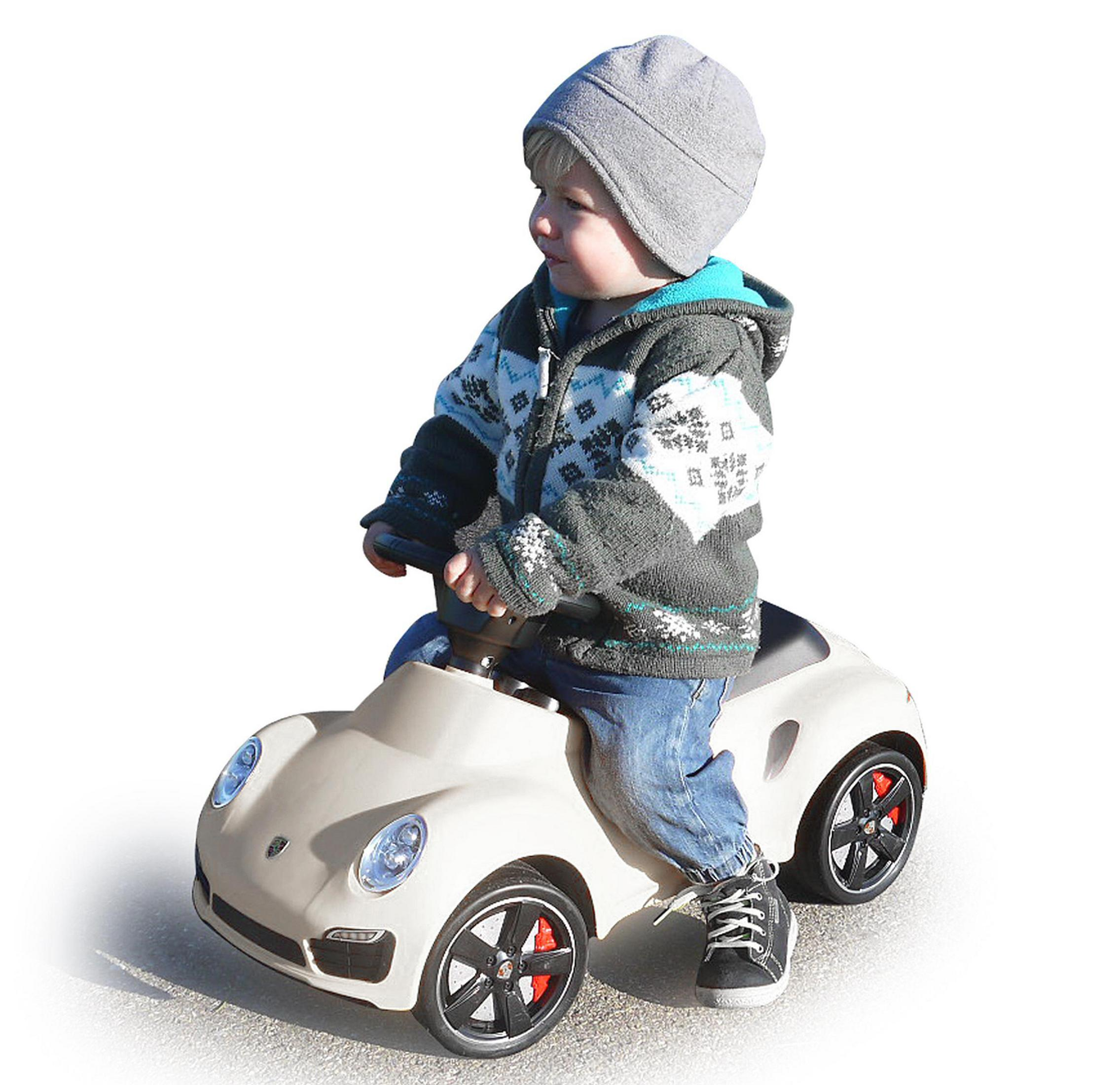 Ein Kind auf einem beigen Spielzeugauto, mit Hut und Jacke.
